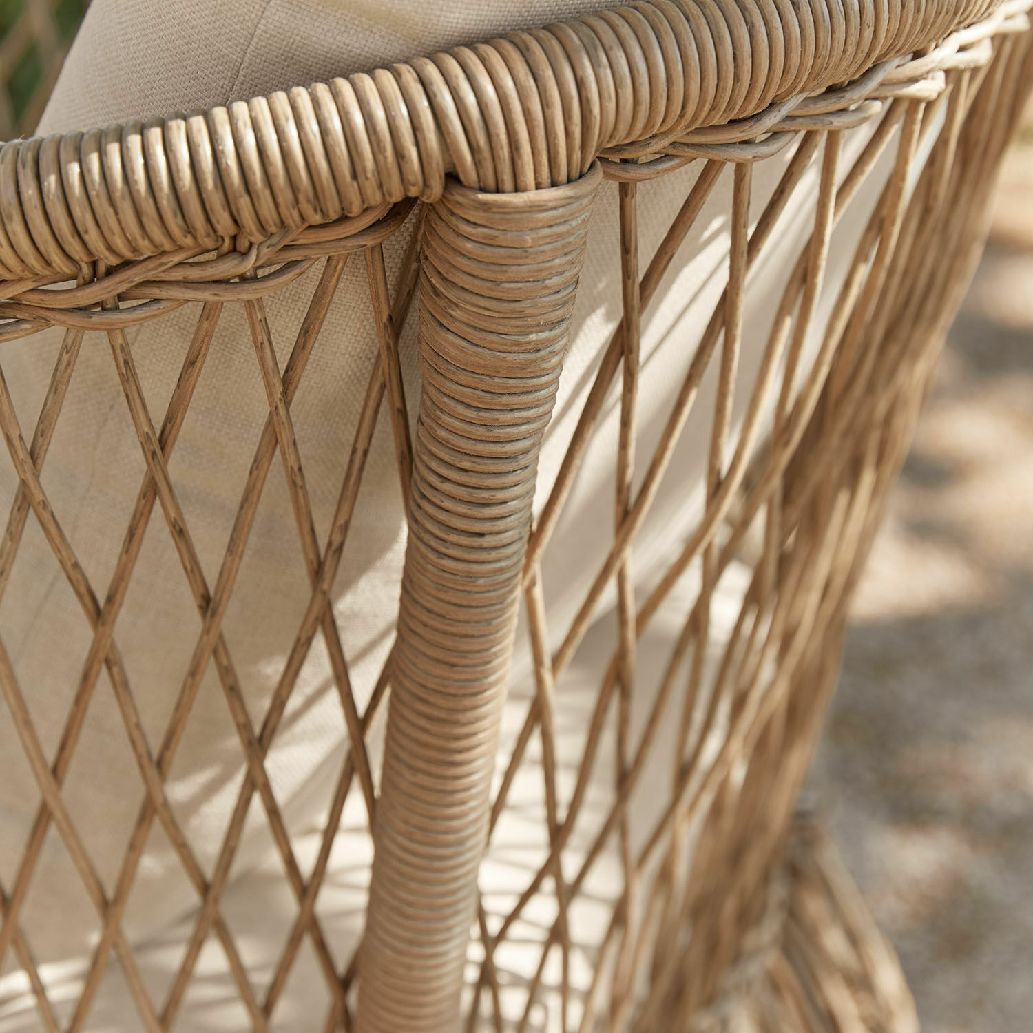 Nahaufnahme eines naturfarbenen Rattanstuhls mit beigem Kissen, Gartenmöbel