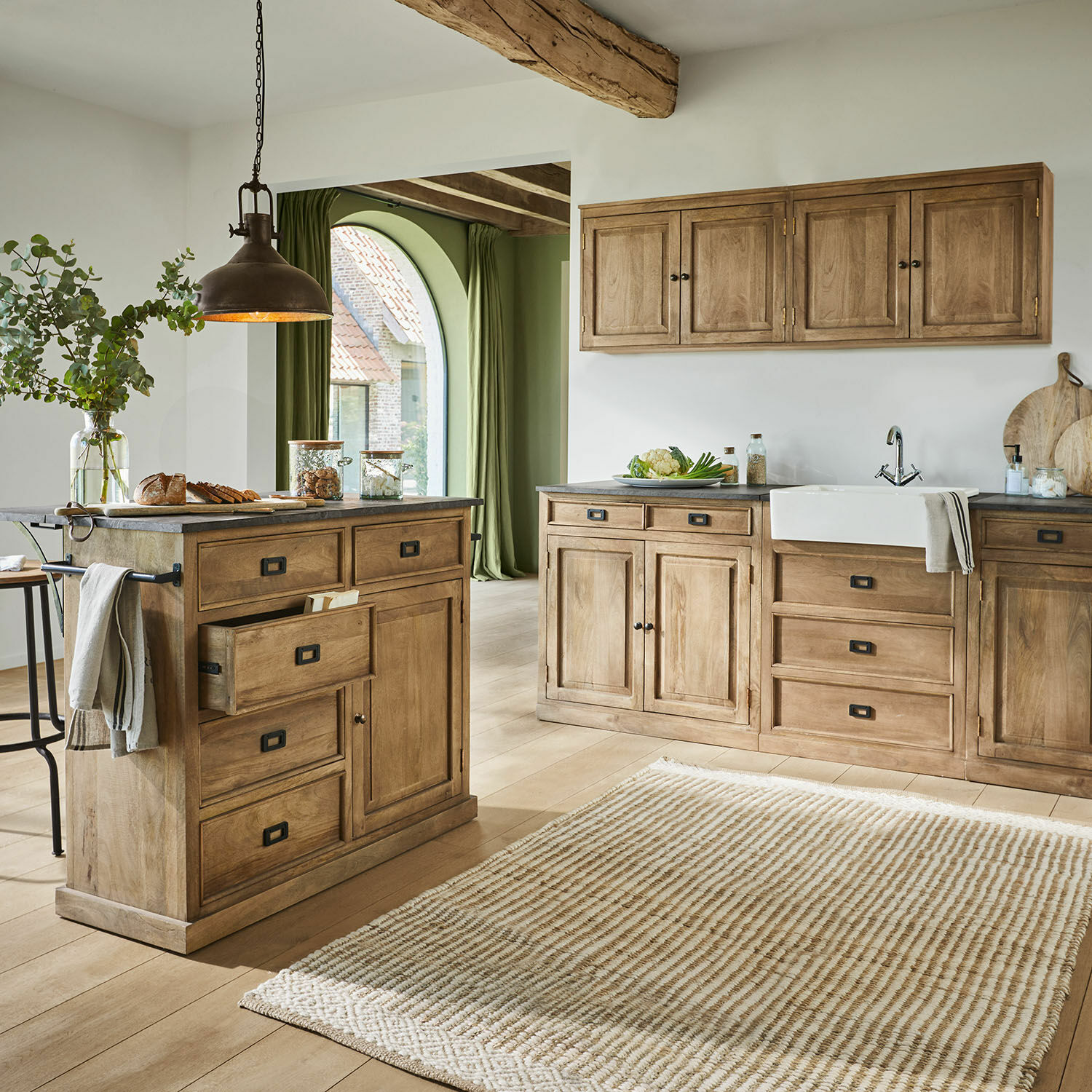 Küche mit naturfarbenen Holzschränken, Kücheninsel, weißem Spülbecken und gestreiftem Teppich.