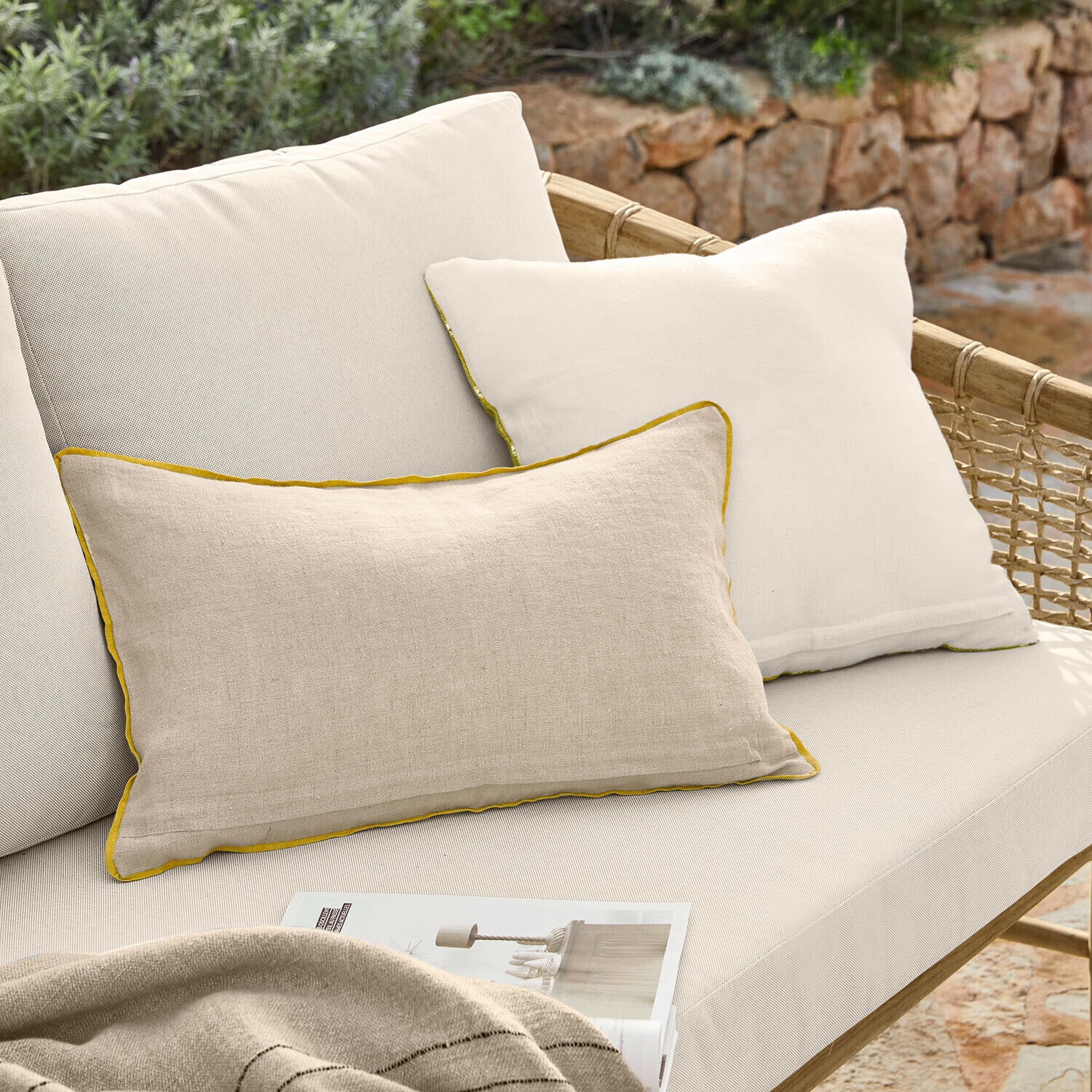 Beige Leinen-Dekokissen mit gelbem Rand auf cremefarbenem Rattansofa im Außenbereich