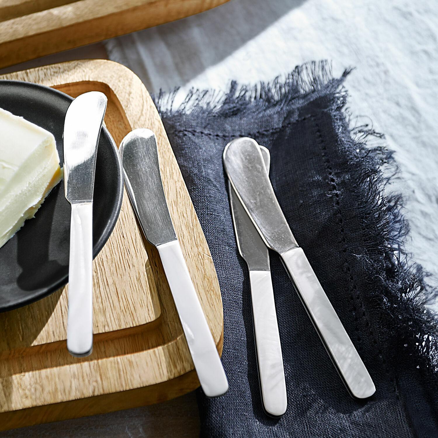 Set aus Edelstahl-Buttermessern mit weißen Griffen auf Holzbrett und dunkelblauem Stoff
