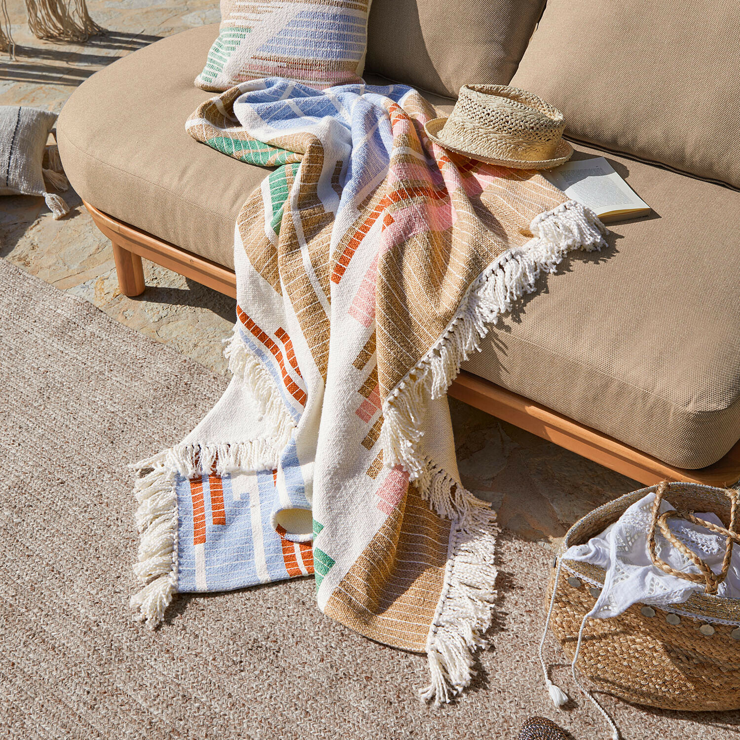 Bunte Baumwolldecke mit Fransen auf beigem Sofa im Außenbereich, dekorativ und gemütlich