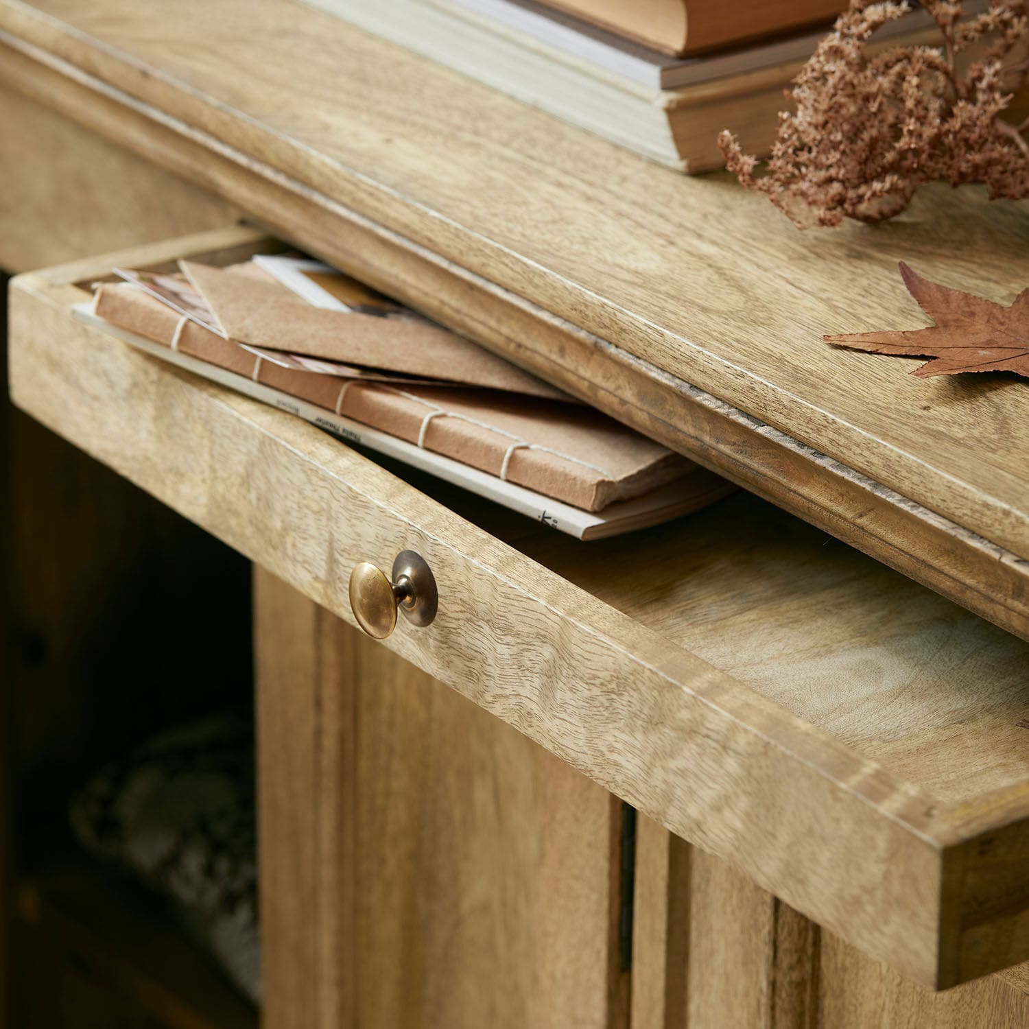 Heller Holzschrank mit geöffneter Schublade, Metallgriff und braunen Notizbüchern darauf