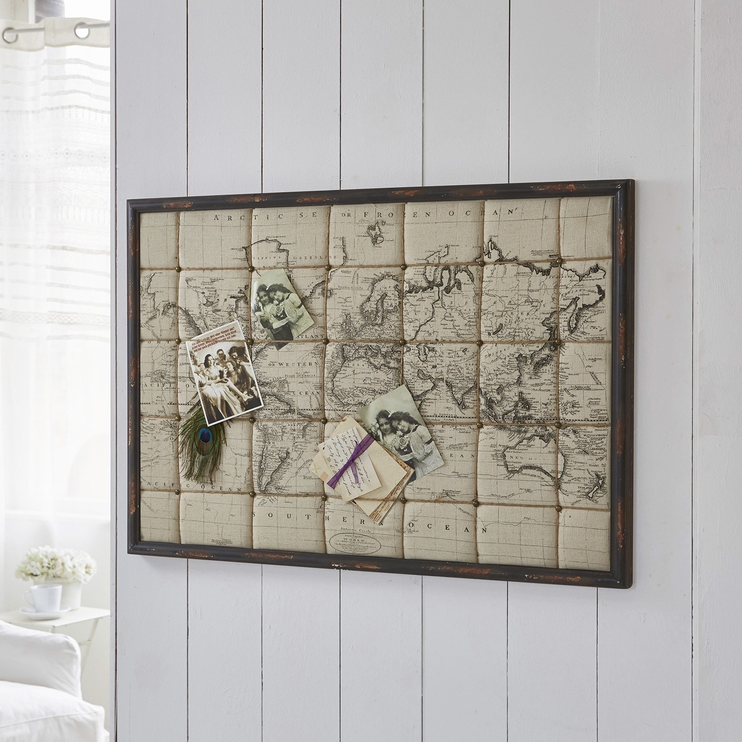 Vintage Pinnwand mit Weltkarte, Fotos und Pfauenfeder in beige-braunen Farbtönen an Wand