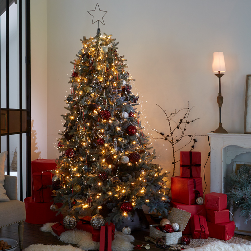 Beleuchteter Weihnachtsbaum mit roten und silbernen Kugeln und roten Geschenken in gemütlichem Wohnzimmer