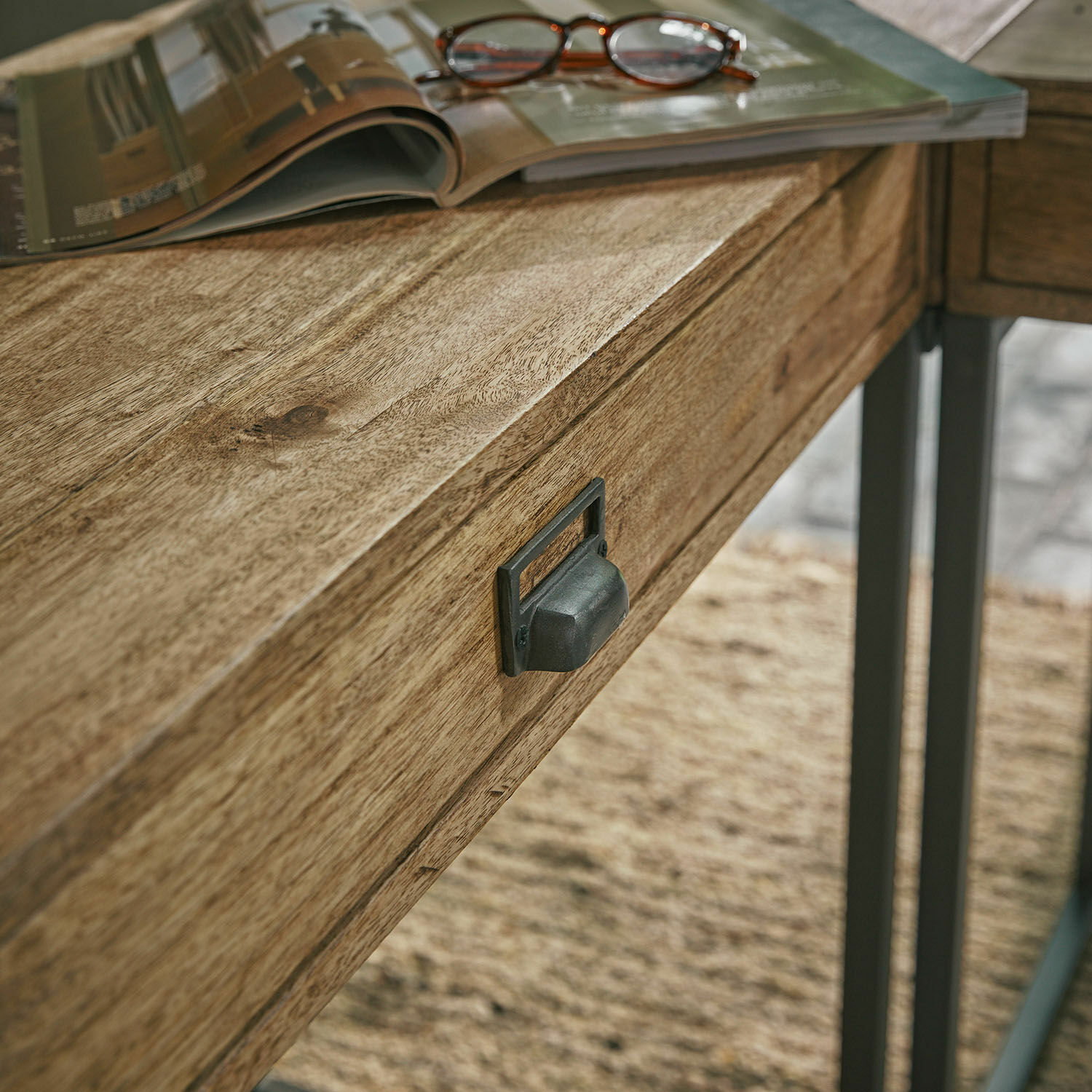 Schreibtischplatte aus natürlichem Mangoholz mit Metallschublade und darauf liegender Brille