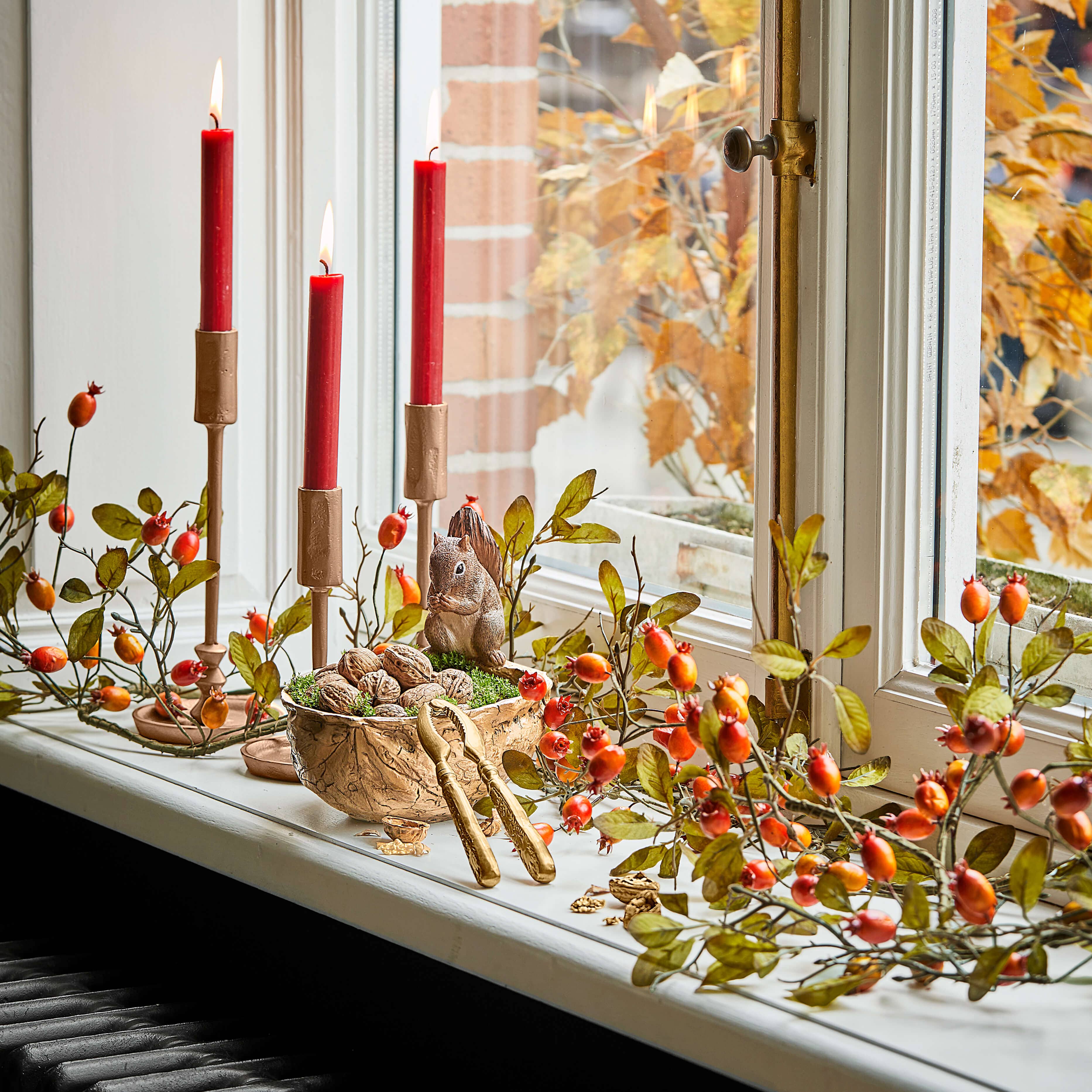 Herbstliche Fensterdekoration mit roten Kerzen, Walnüssen und Eichhörnchenfigur auf Fensterbank