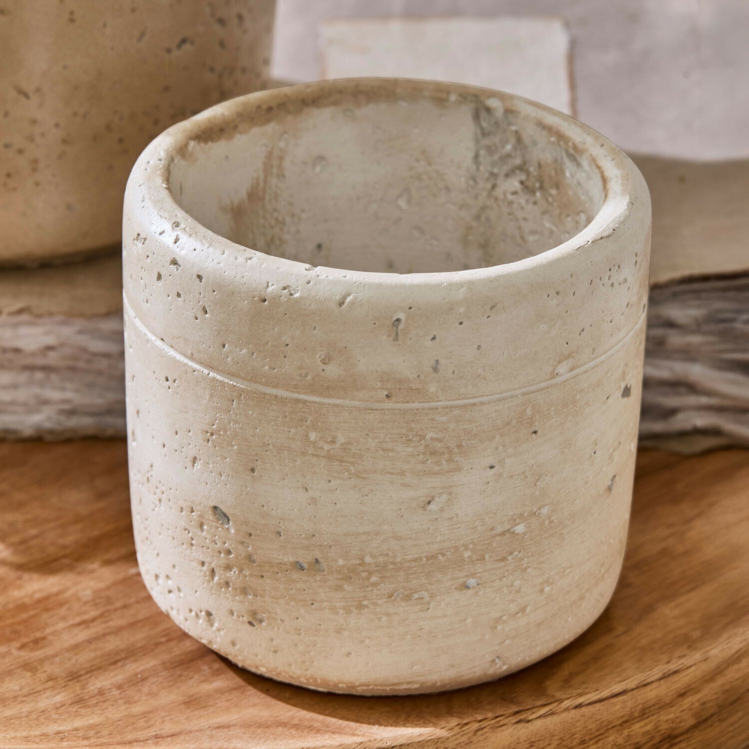 Runder Blumentopf aus hellem Beton mit rauer Oberfläche auf Holztisch für Wohnraumdekoration