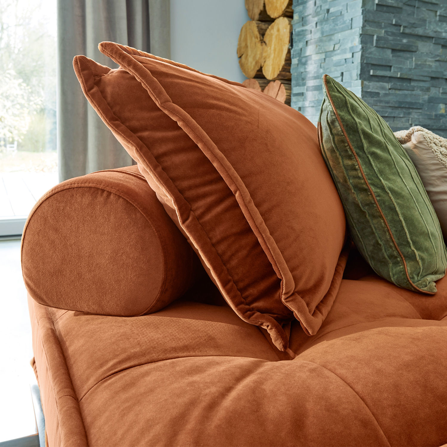 Braunes Samtsofa mit Kissen und Nackenrolle in gemütlichem Wohnzimmer mit Kamin