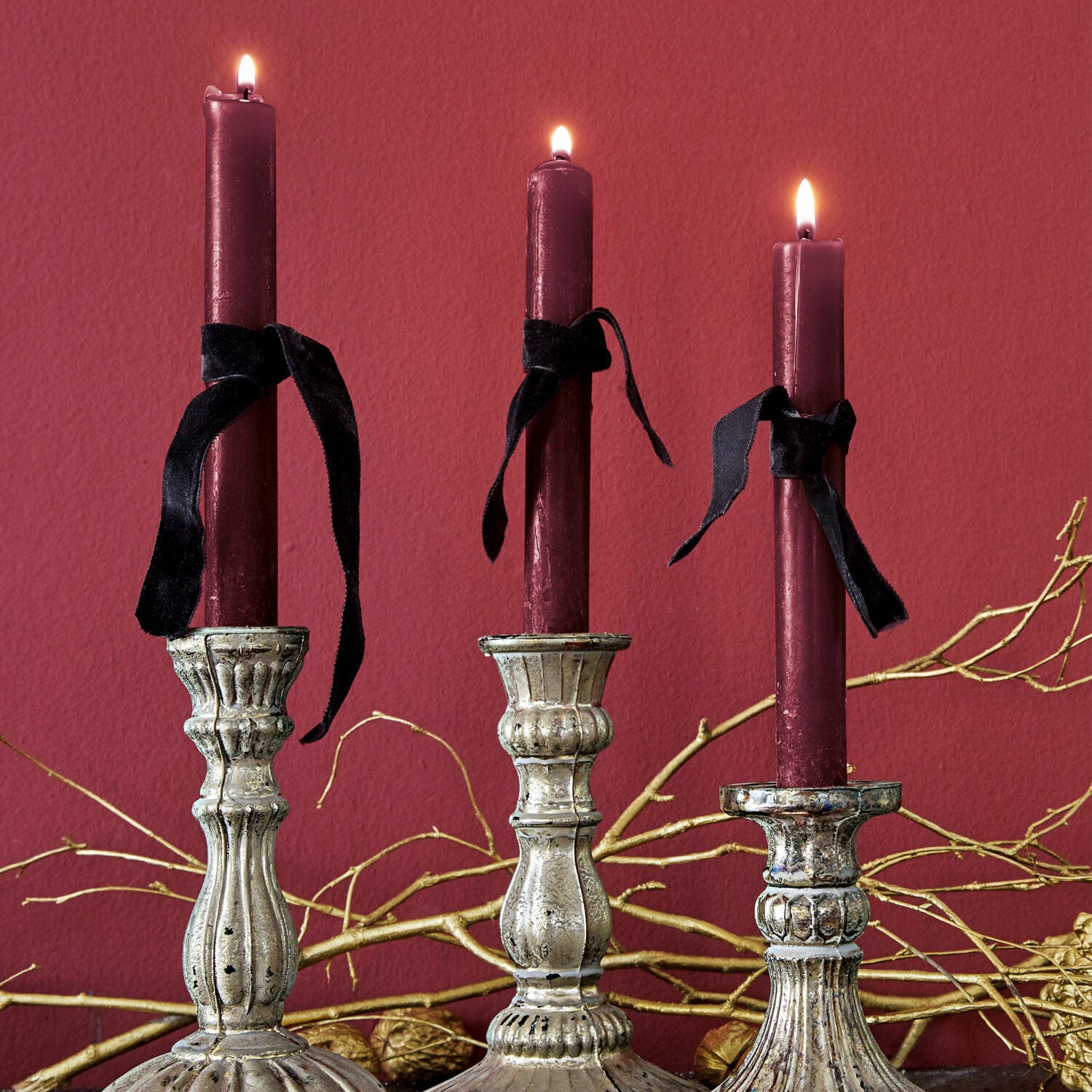 Kerze 12er Set Bauceau Drei silberne Metallkerzenhalter mit bordeauxfarbenen Kerzen und schwarzen Bändern vor rotem Hintergrund
