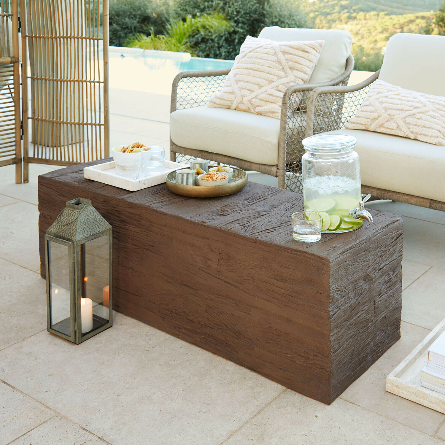 Brauner Couchtisch mit Holzstruktur auf Terrasse mit cremefarbenen Kissen und Zitronenlimonade