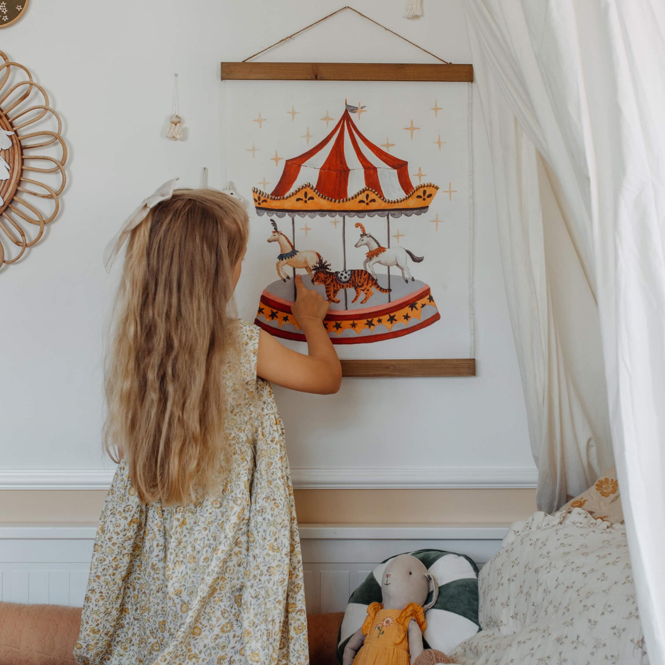 Mädchen zeigt auf ein Karussellbild mit Pferden im Kinderzimmer mit Plüschtier und hellem Dekor