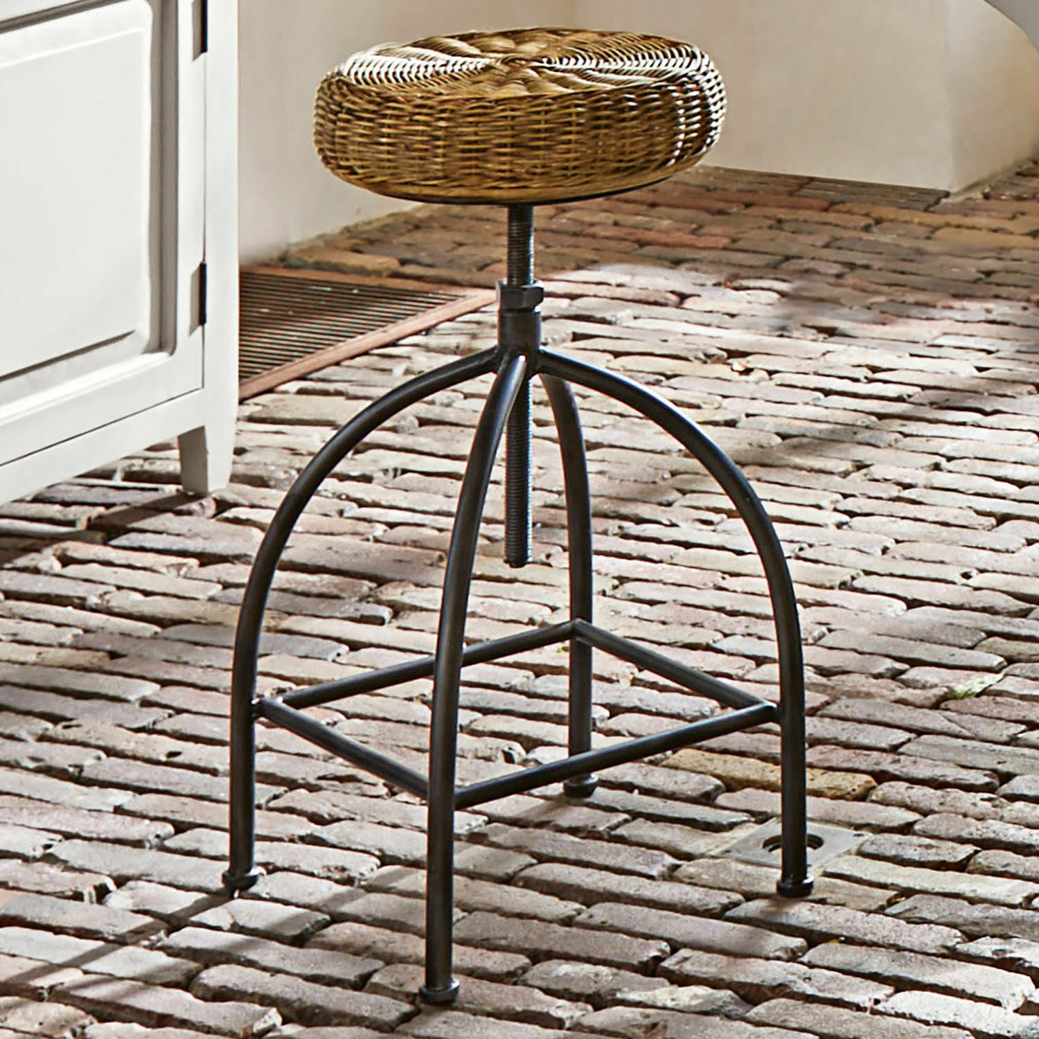 Hocker mit schwarzem Metallgestell und rundem Sitz aus Korbgeflecht auf Ziegelboden