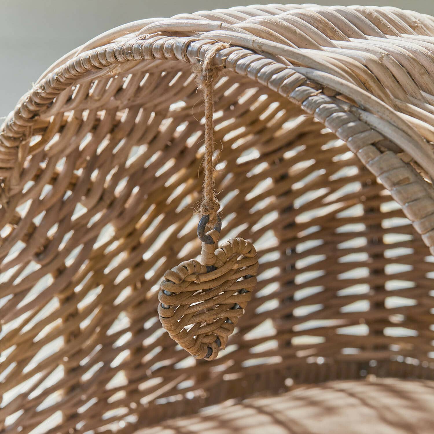 Dekoratives Herz aus natürlichem Rattan an einem hellbeigen, geflochtenen Rattanmöbel