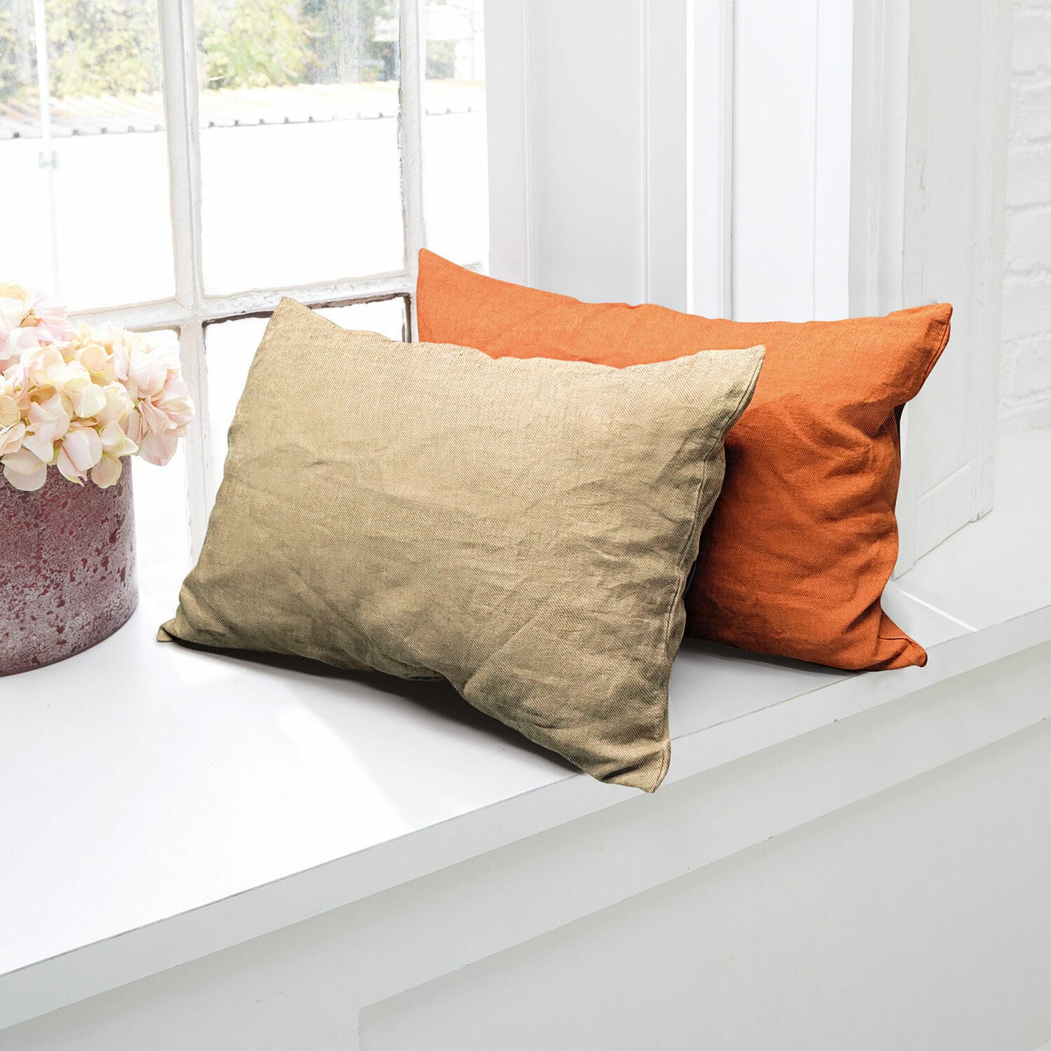 Zwei dekorative Kissen aus Stoff in Beige und Orange auf weißem Fensterbrett