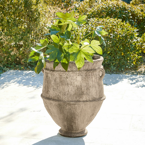 Großer grauer Steintopf mit grüner Pflanze auf hellem Terrassenboden, Gartendekor
