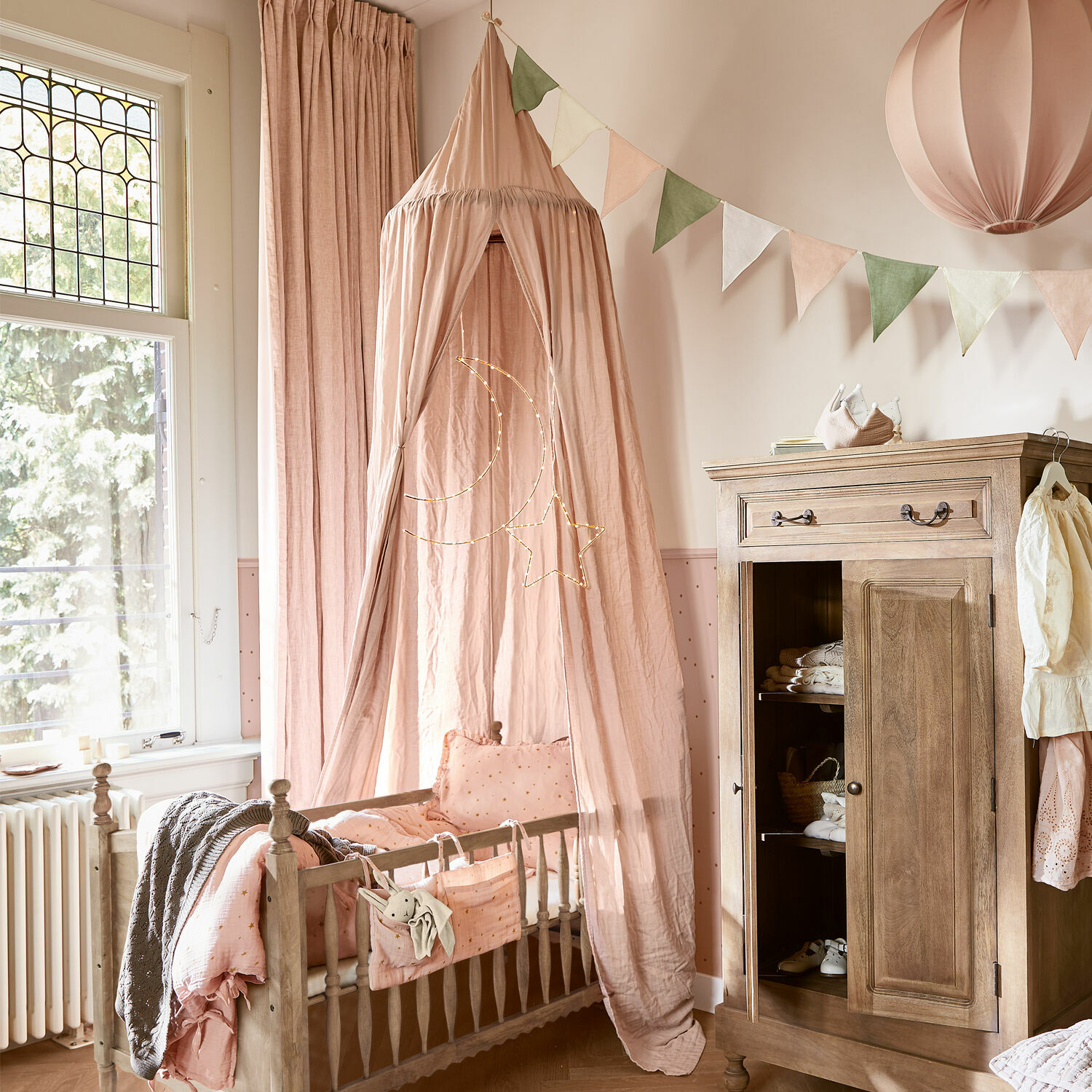 Kinderbett aus Holz mit rosa Baldachin und Mond-Stern-Dekoration in einem hellen Kinderzimmer