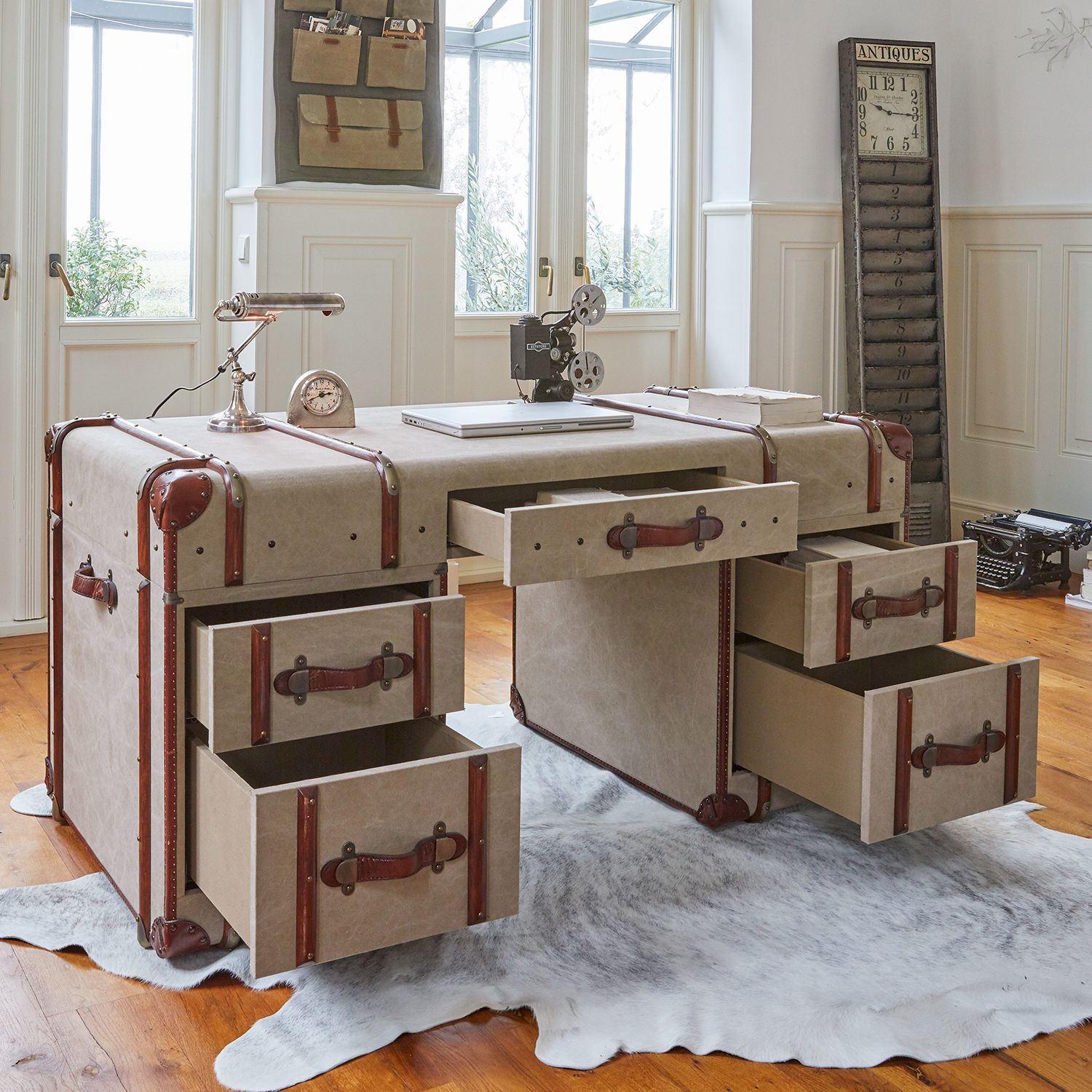Vintage Schreibtisch aus beigem Material mit braunen Ledergriffen, offenen Schubladen und Retro-Dekor im hellen Raum