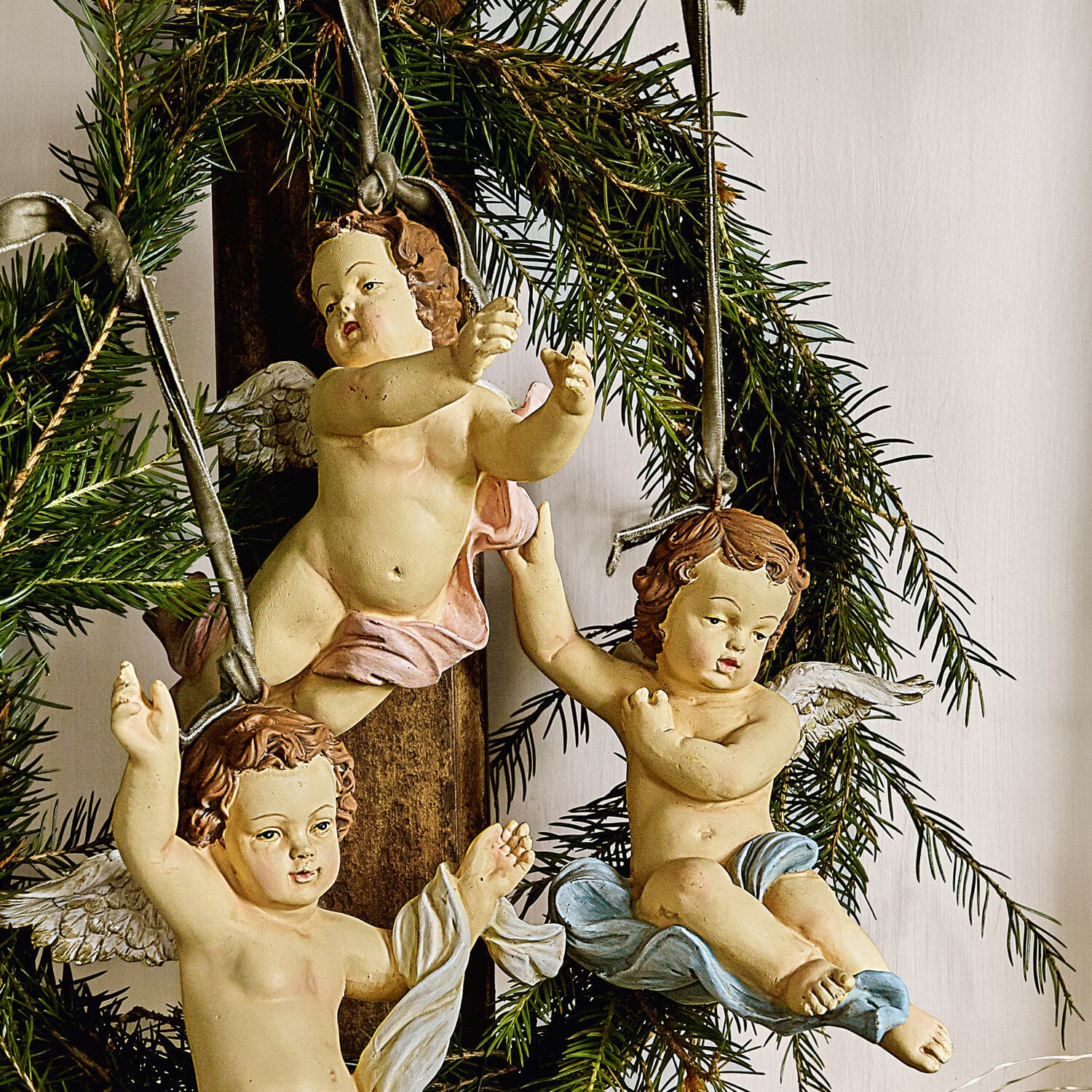 Drei hängende Engel aus Kunststoff mit pastellfarbenen Gewändern vor Tannenzweigen, Weihnachtsdeko
