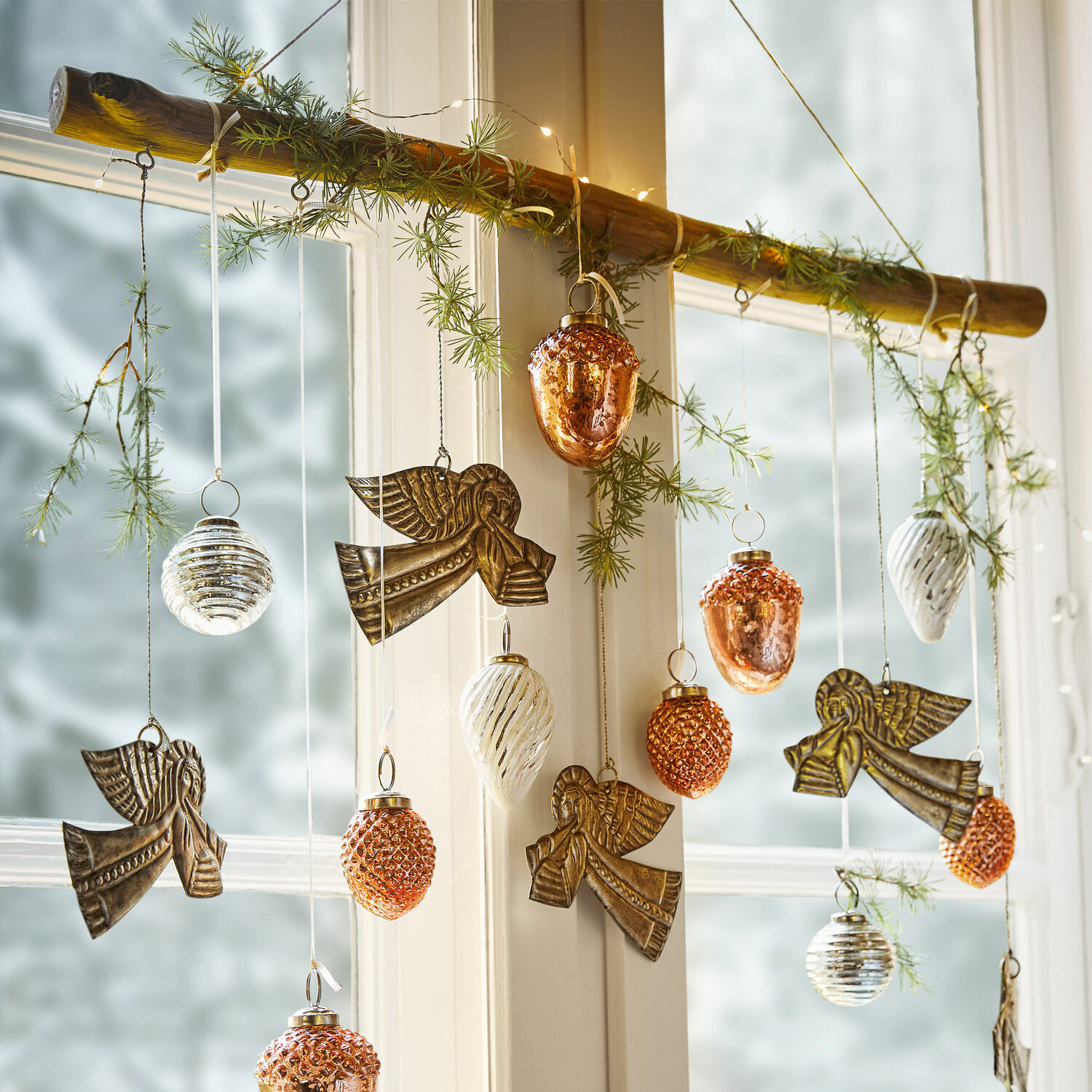 Weihnachtsdeko mit Metallengeln und kupfer-weißen Glasornamenten an einem Holzast hängend