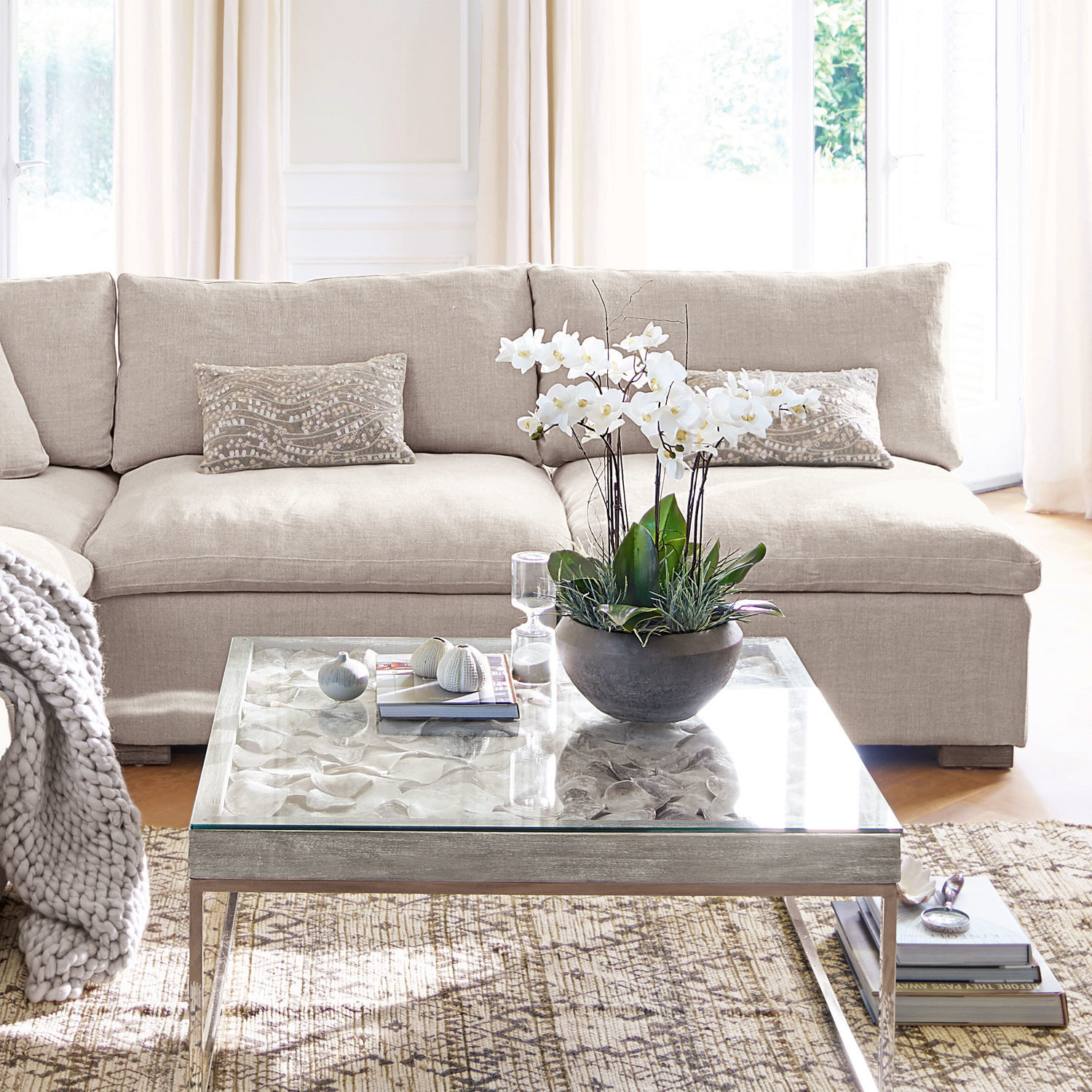 Sessel Bennington Beiges Stoffsofa mit dekorativen Kissen und Glastisch mit weißer Blume im Wohnzimmer