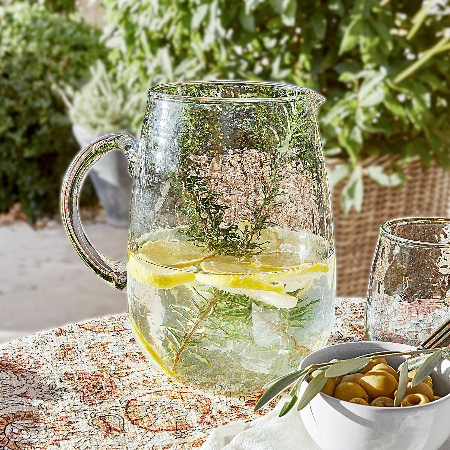 Krug Rezay Glaskrug mit Wasser, Zitrone und Kräutern auf gemustertem Tischtuch, erfrischendes Sommergetränk