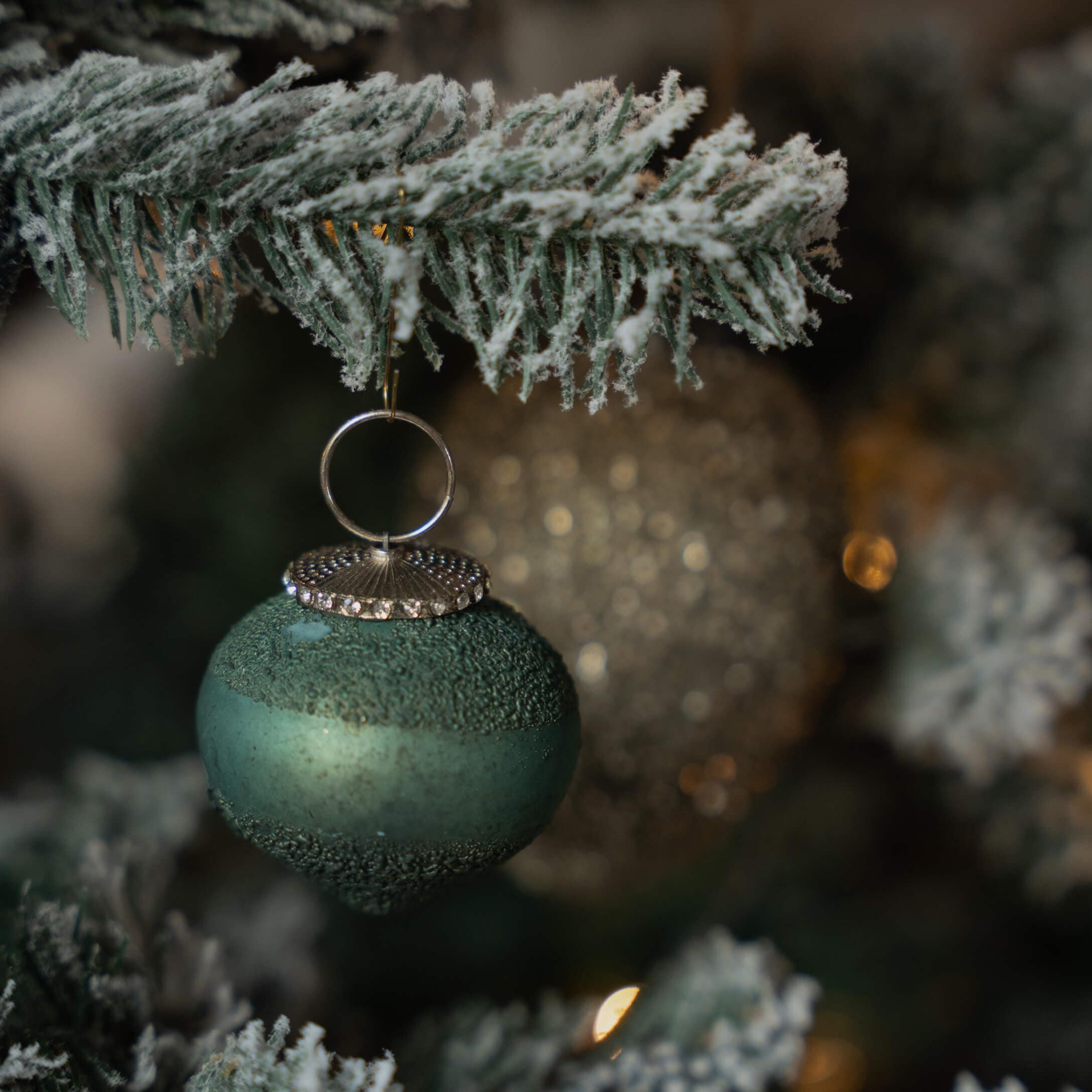 Grüne matte Weihnachtsbaumkugel mit strukturierter Oberfläche und silberner Aufhängung an verschneigtem Zweig