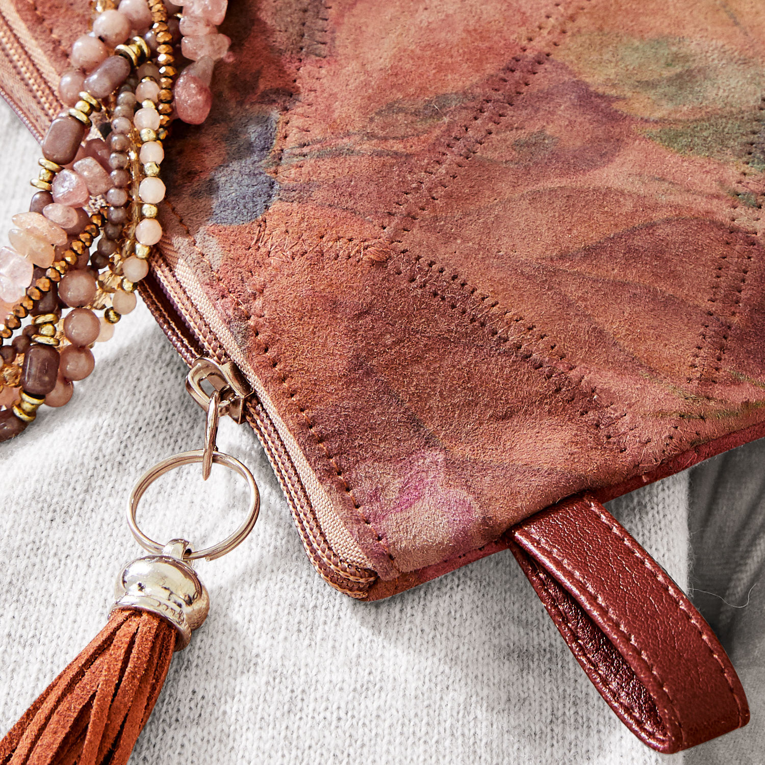 Braune Wildledertasche mit Quaste und dekorativem Reißverschluss, modisches Accessoire aus Naturleder.