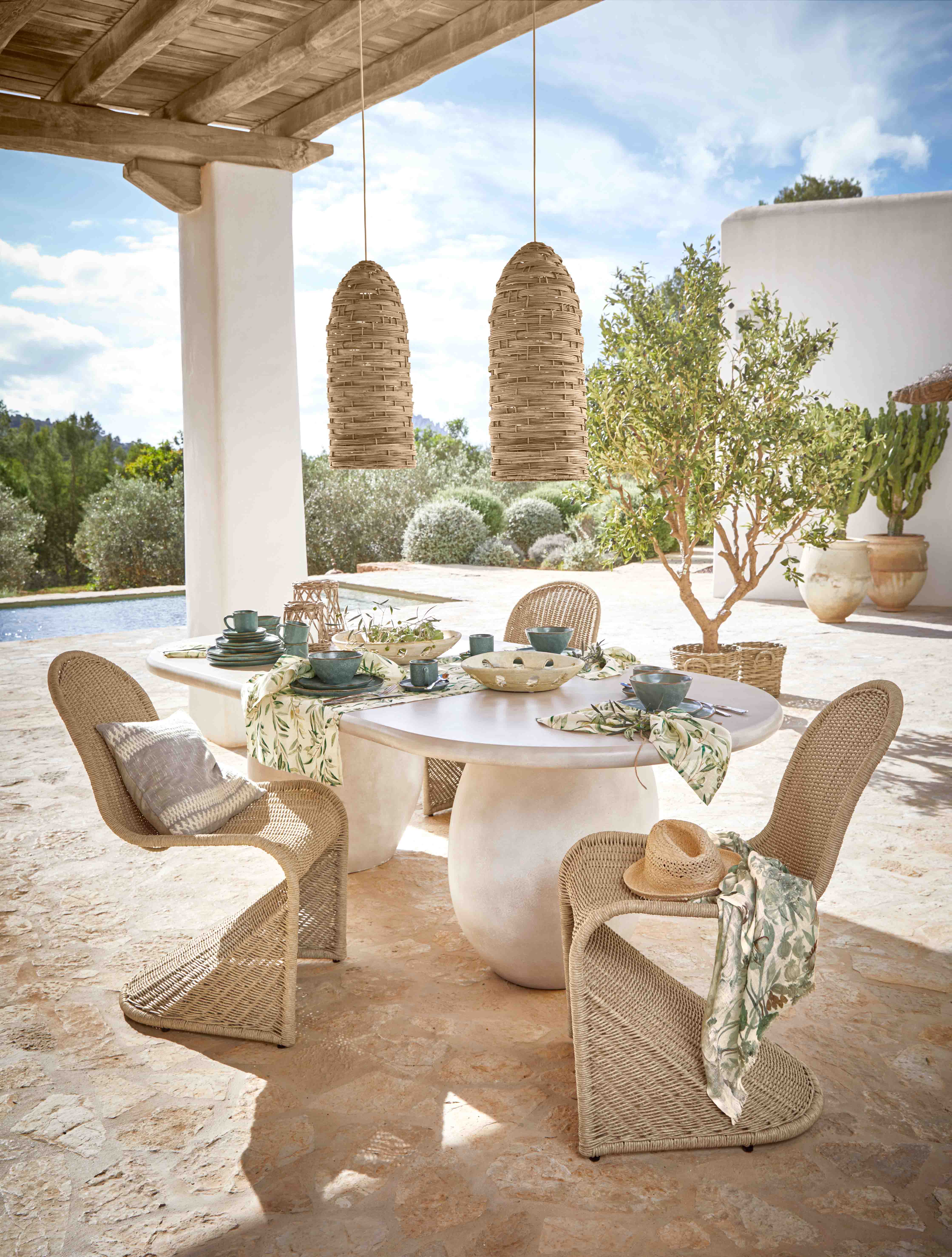 Gartenmöbel-Set mit geflochtenen Stühlen und weißem Tisch auf Terrasse mit Tischdekoration