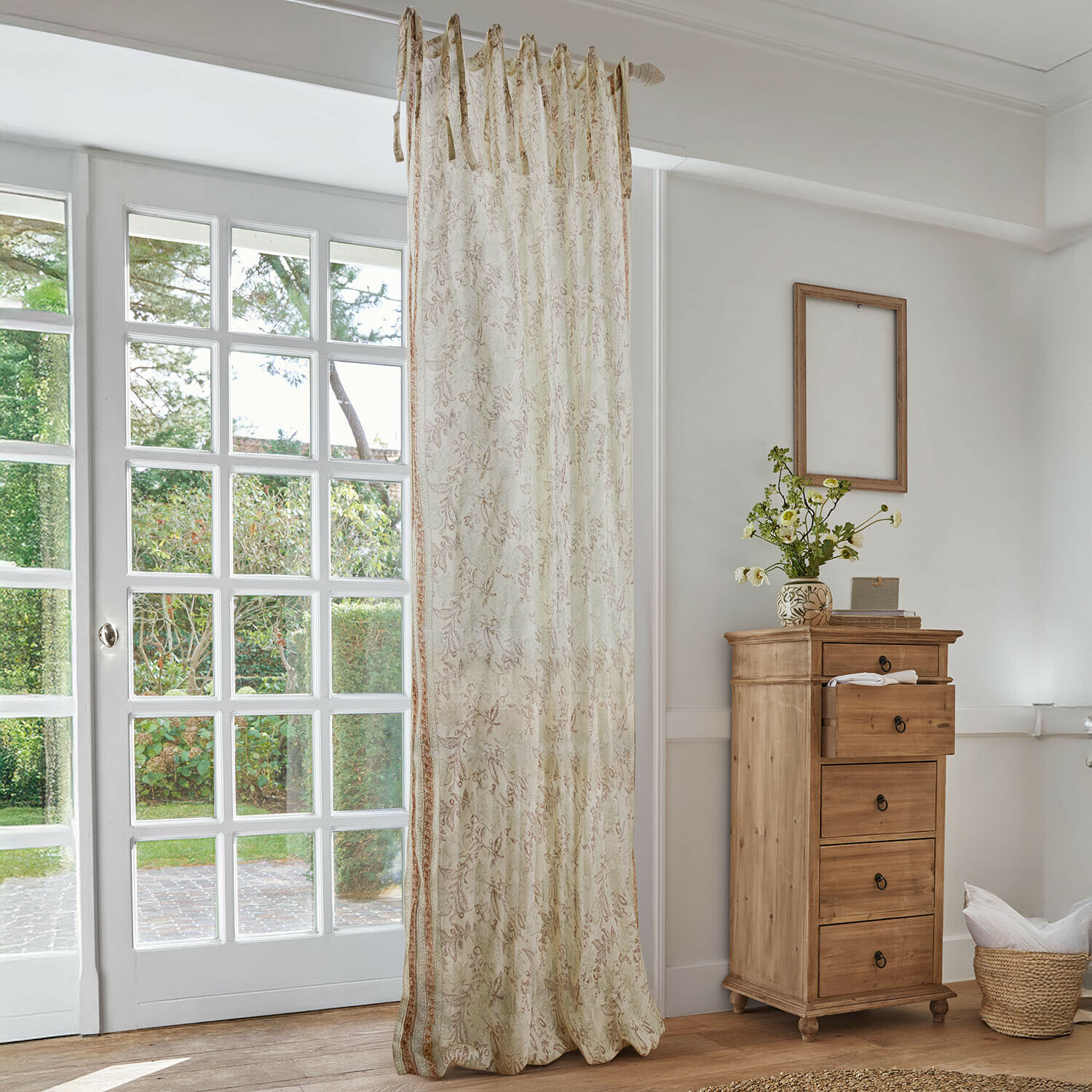 Beiger Vorhang mit zartem Blumenmuster in hellem Wohnzimmer mit Holzkommode und großem Fenster