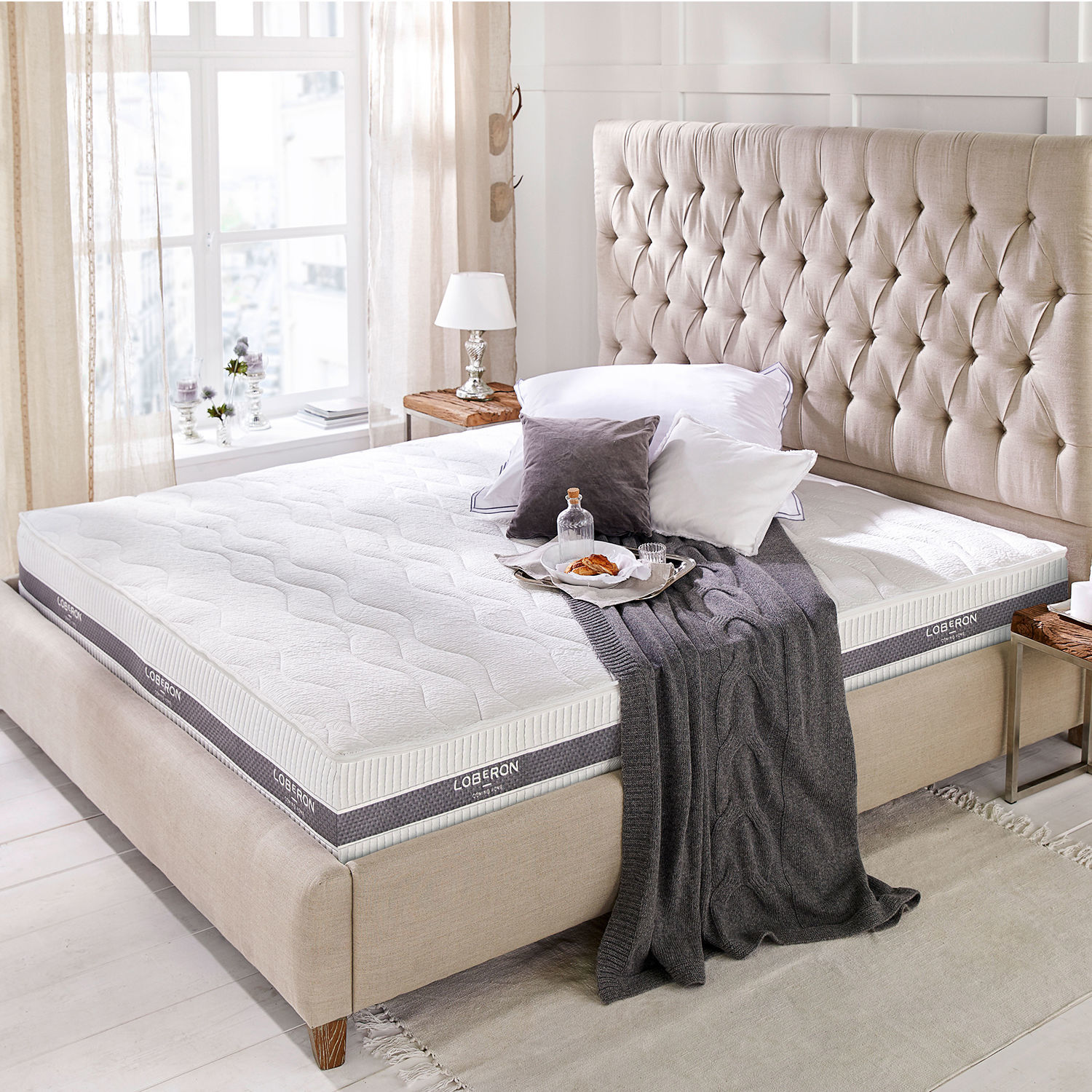 Matratze 180x200 Turim Moderner weißer Loberon-Matratze auf beige gepolstertem Bett mit gestepptem Kopfteil im hellen Raum