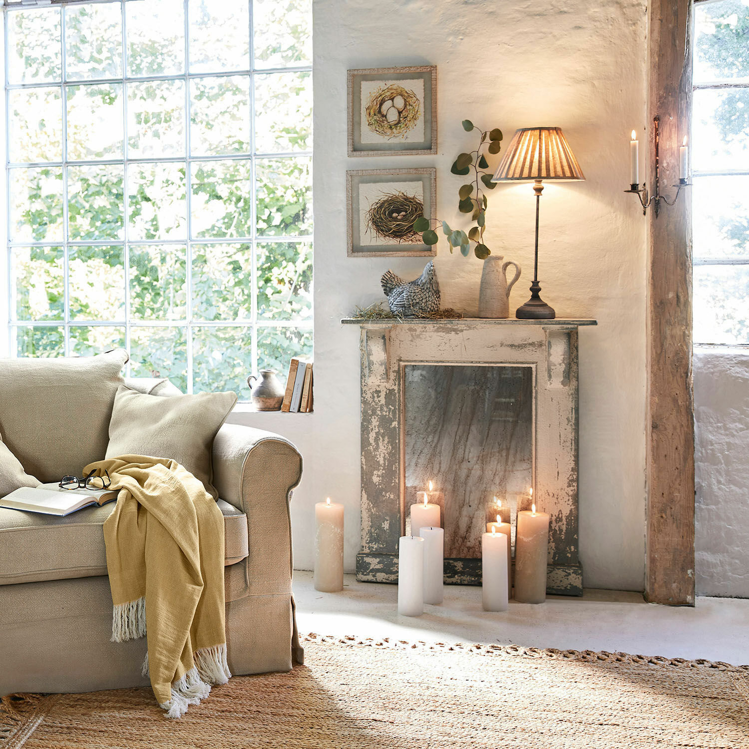 Gemütliches Wohnzimmer mit beigem Sofa, gelber Decke und brennenden Kerzen auf rustikalem Vintage-Kamin