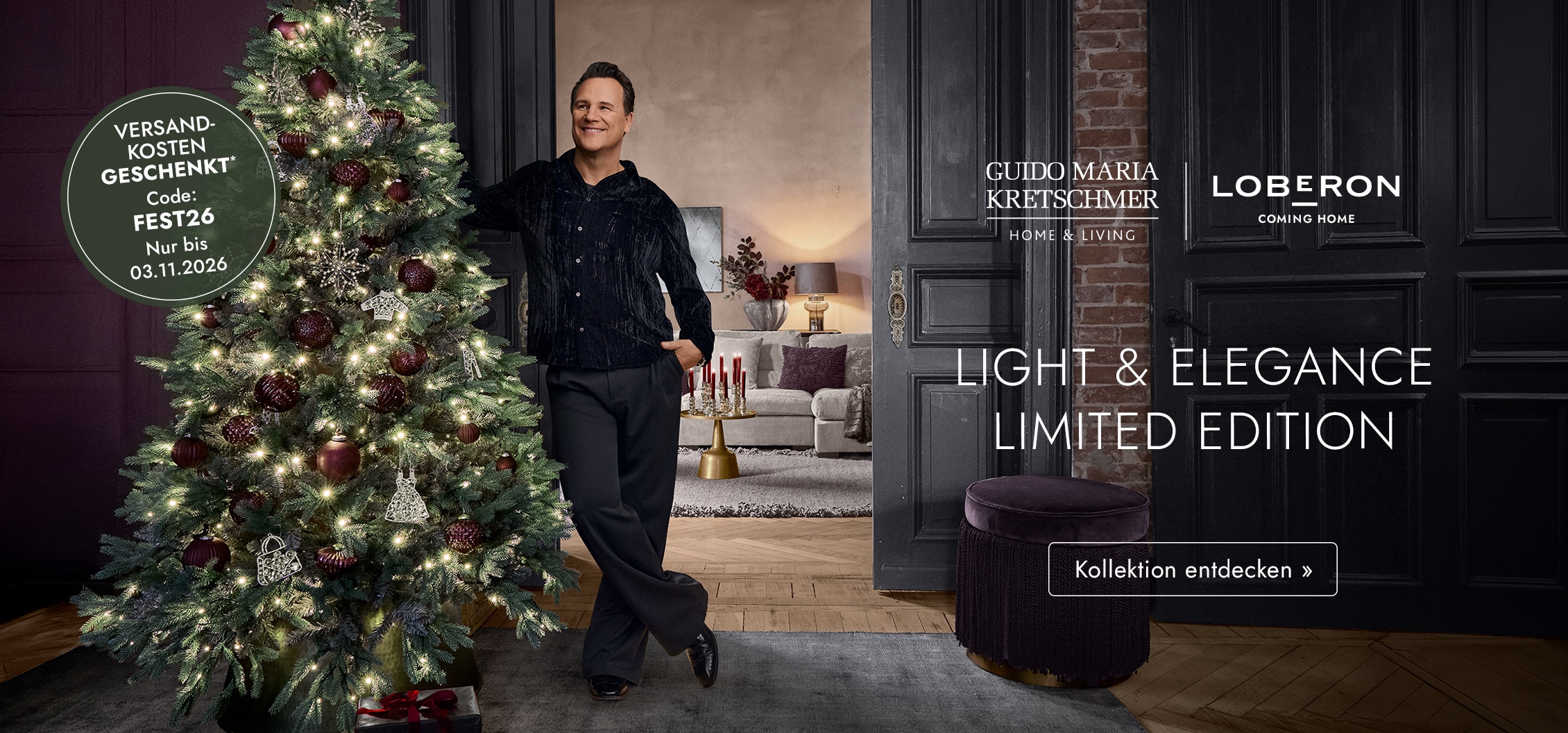 Mann lehnt an beleuchtetem Weihnachtsbaum mit bordeauxfarbenen Kugeln in elegantem Wohnzimmer
