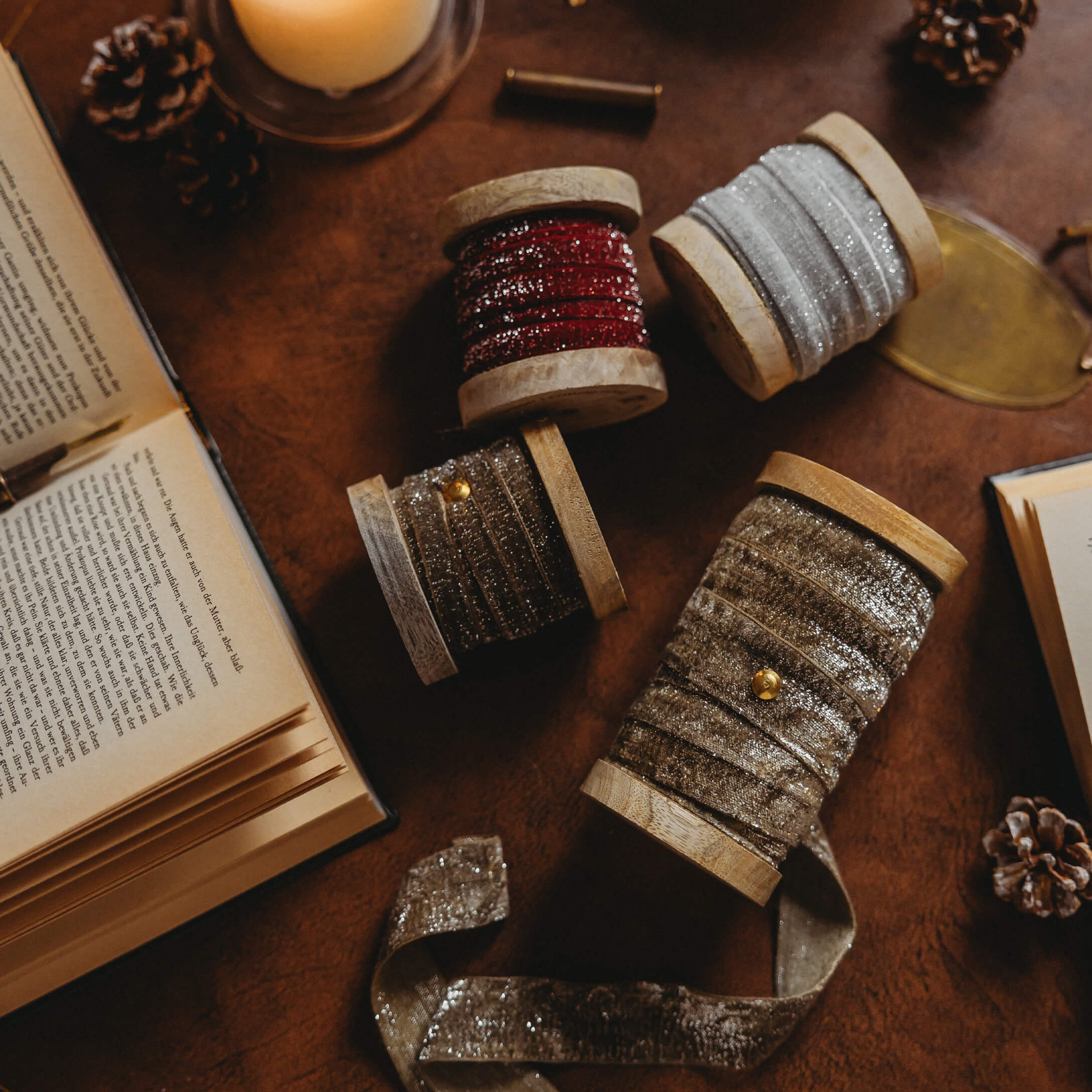 Holzspulen mit glitzernden Bändern in Rot, Silber und Gold auf Tisch mit Büchern