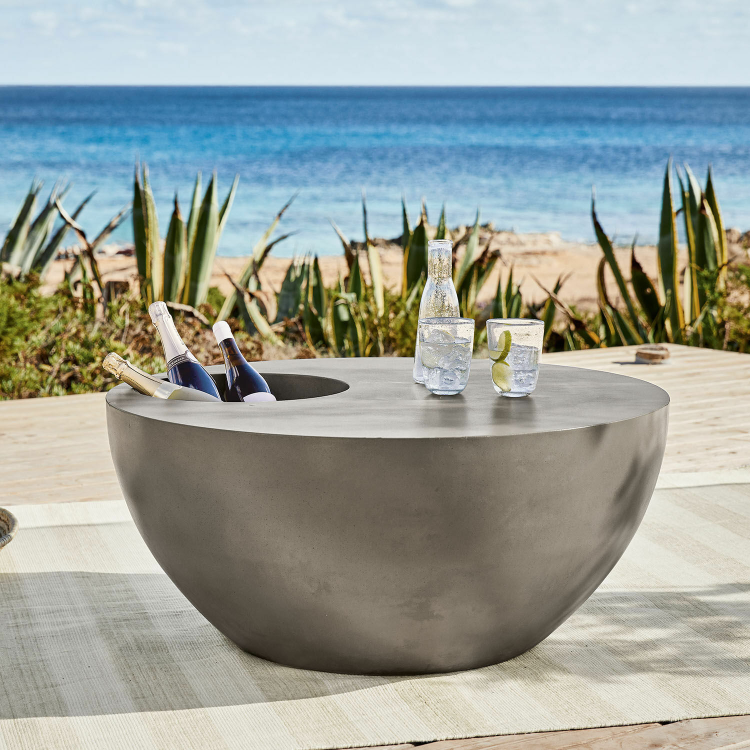 Runder grauer Betontisch mit integriertem Flaschenfach, ideal für Terrasse am Meer