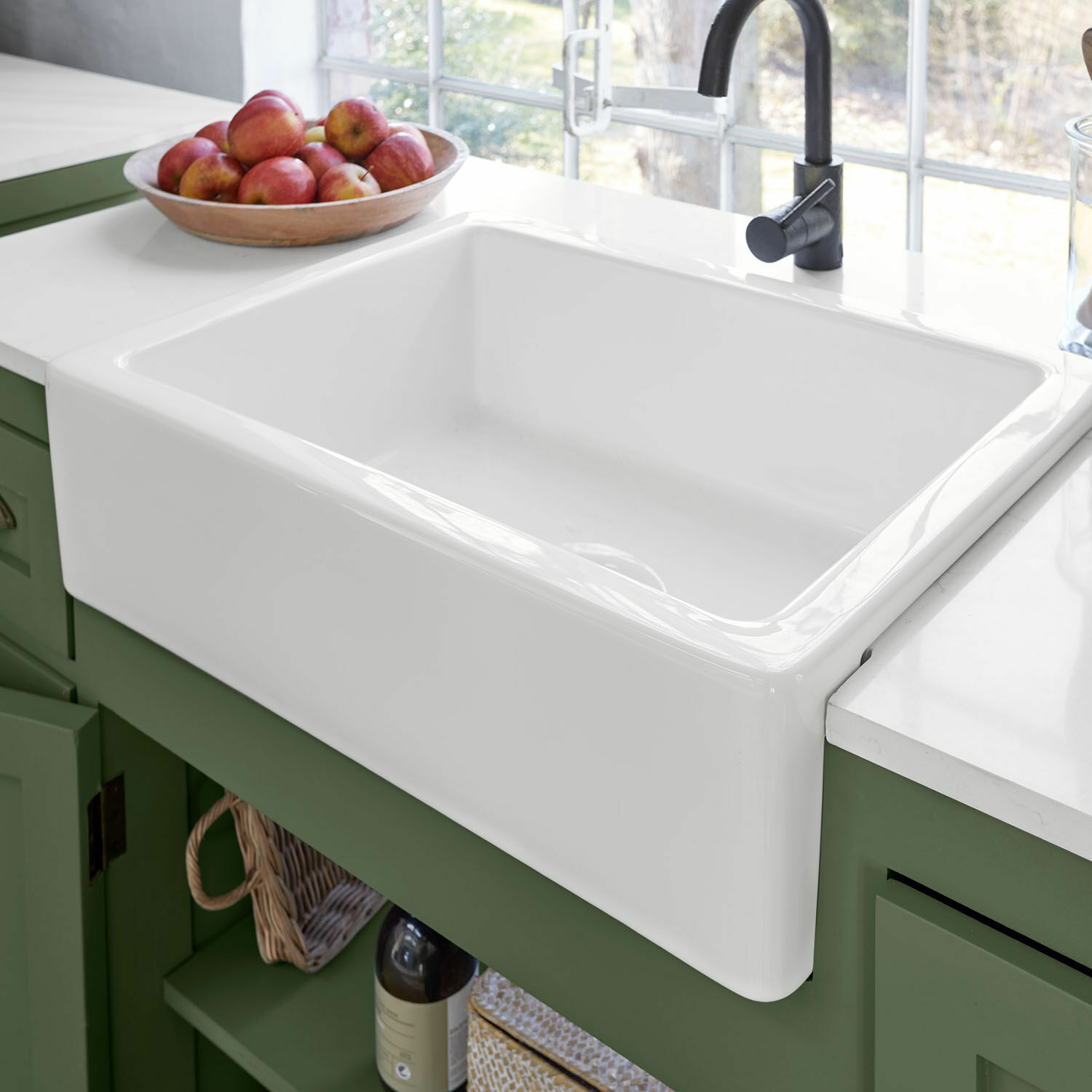 Weißer Keramikspülbecken mit schwarzem Wasserhahn auf grünem Küchenschrank und Apfelschale