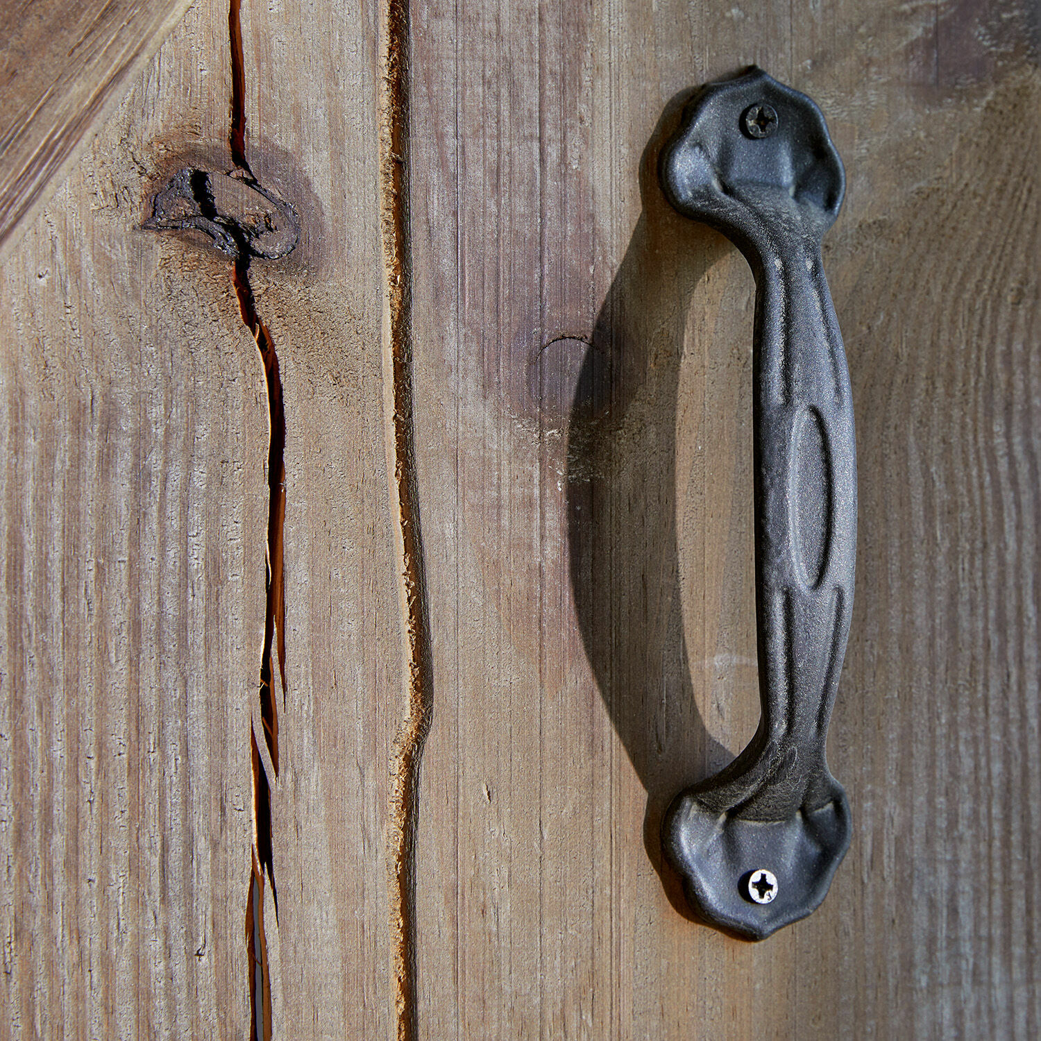 Schwarzer Metallgriff an Holztür mit sichtbaren Rissen und Holzmaserung