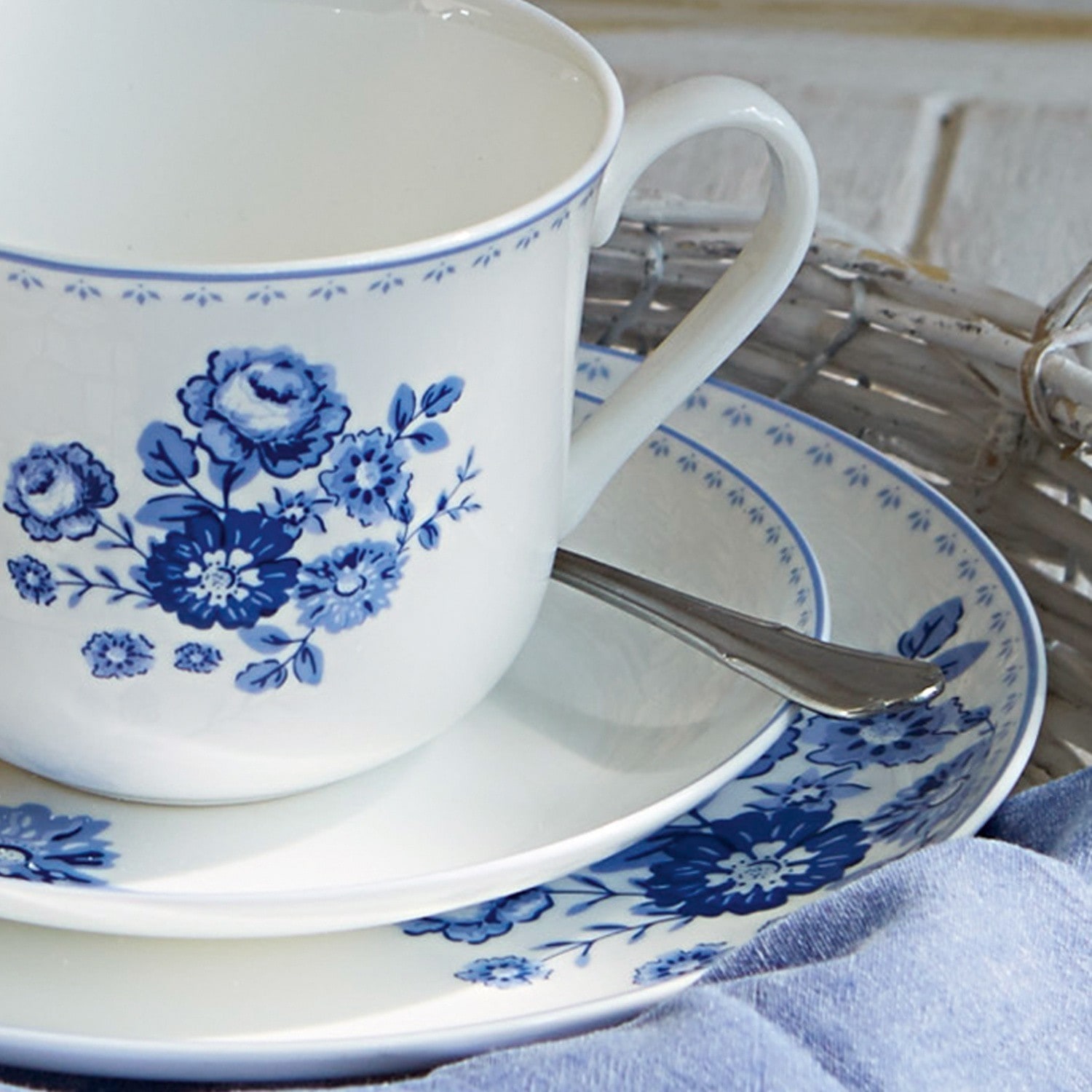 Weißer Porzellanbecher und Teller mit blauem Blumenmuster für den Kaffeetisch