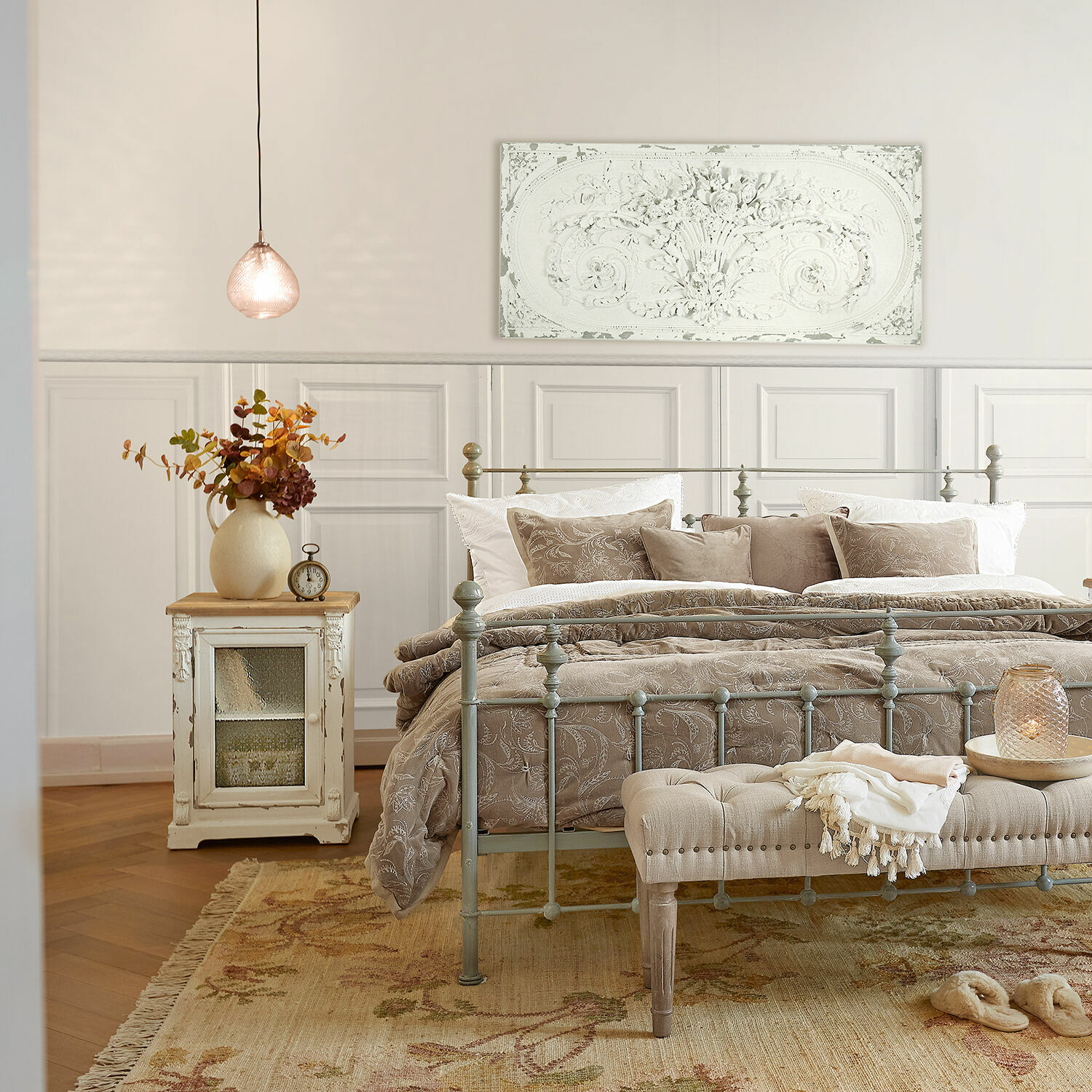 Schlafzimmer mit Metallbett, beiger Bettwäsche und rustikalem Nachttisch mit Blumenarrangement