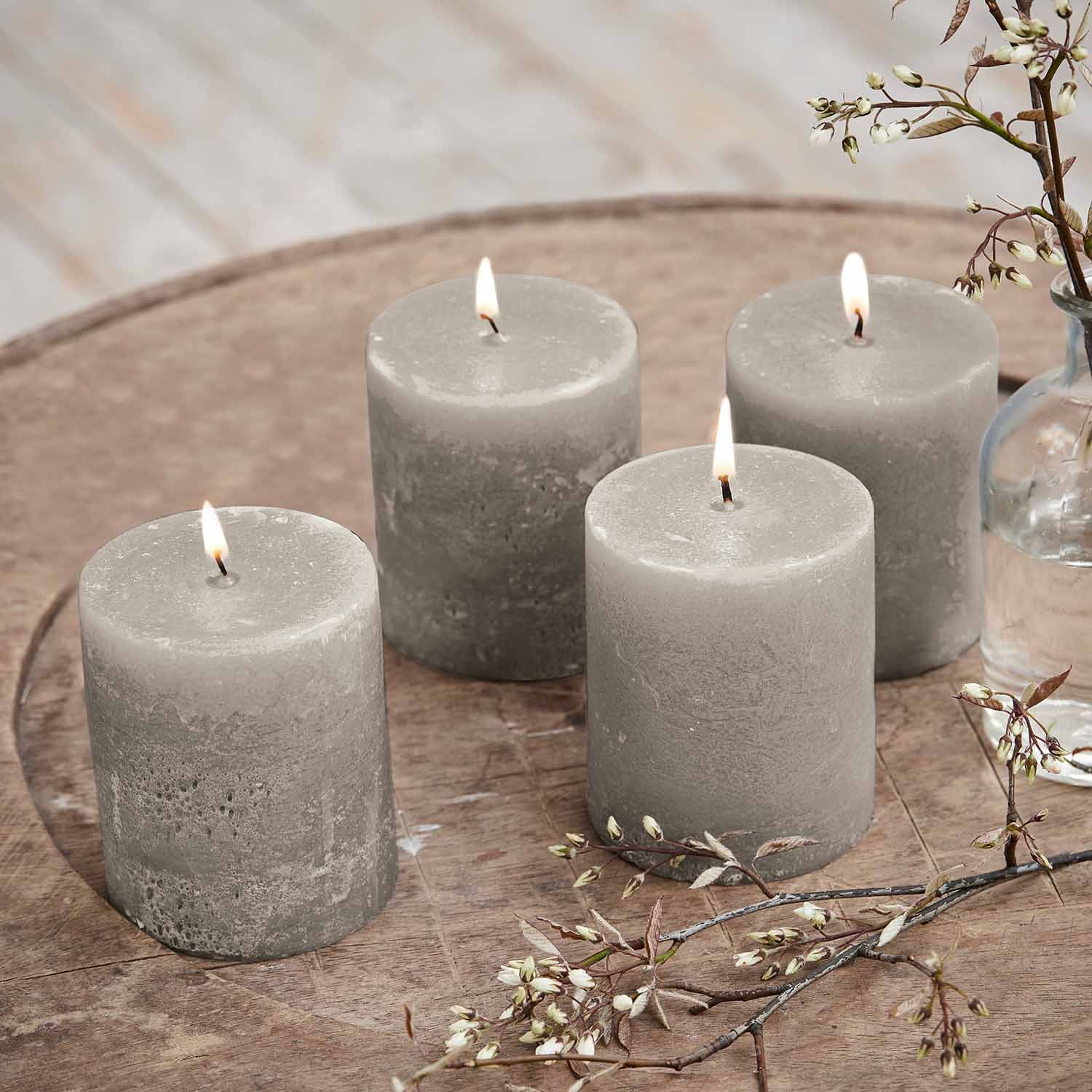 Vier graue Wachskerzen auf Holztisch mit zarter Blumen-Dekoration, Wohnaccessoire