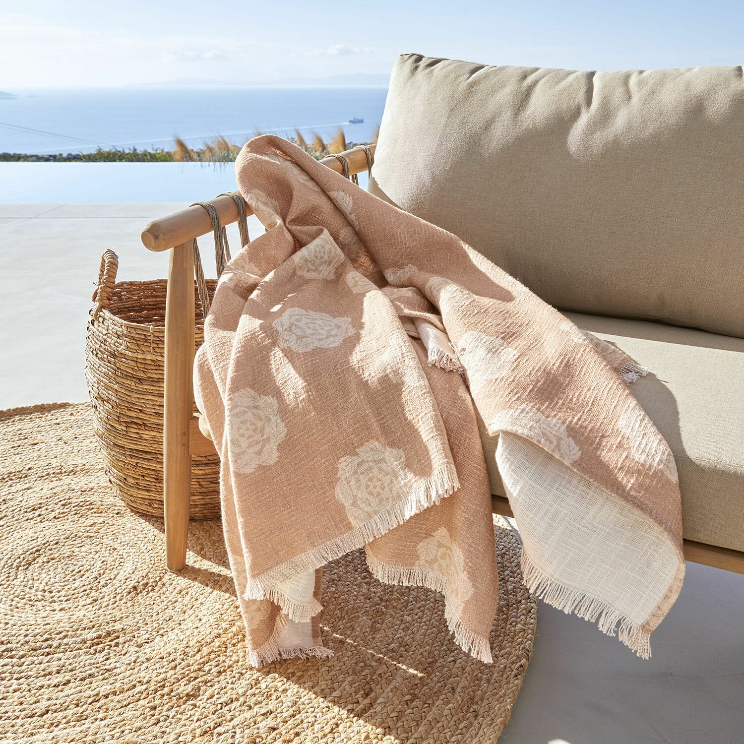 Plaid Belvienne Beige Decke mit weißem Blumenmuster aus weichem Stoff auf Holzstuhl auf Terrasse mit Meerblick