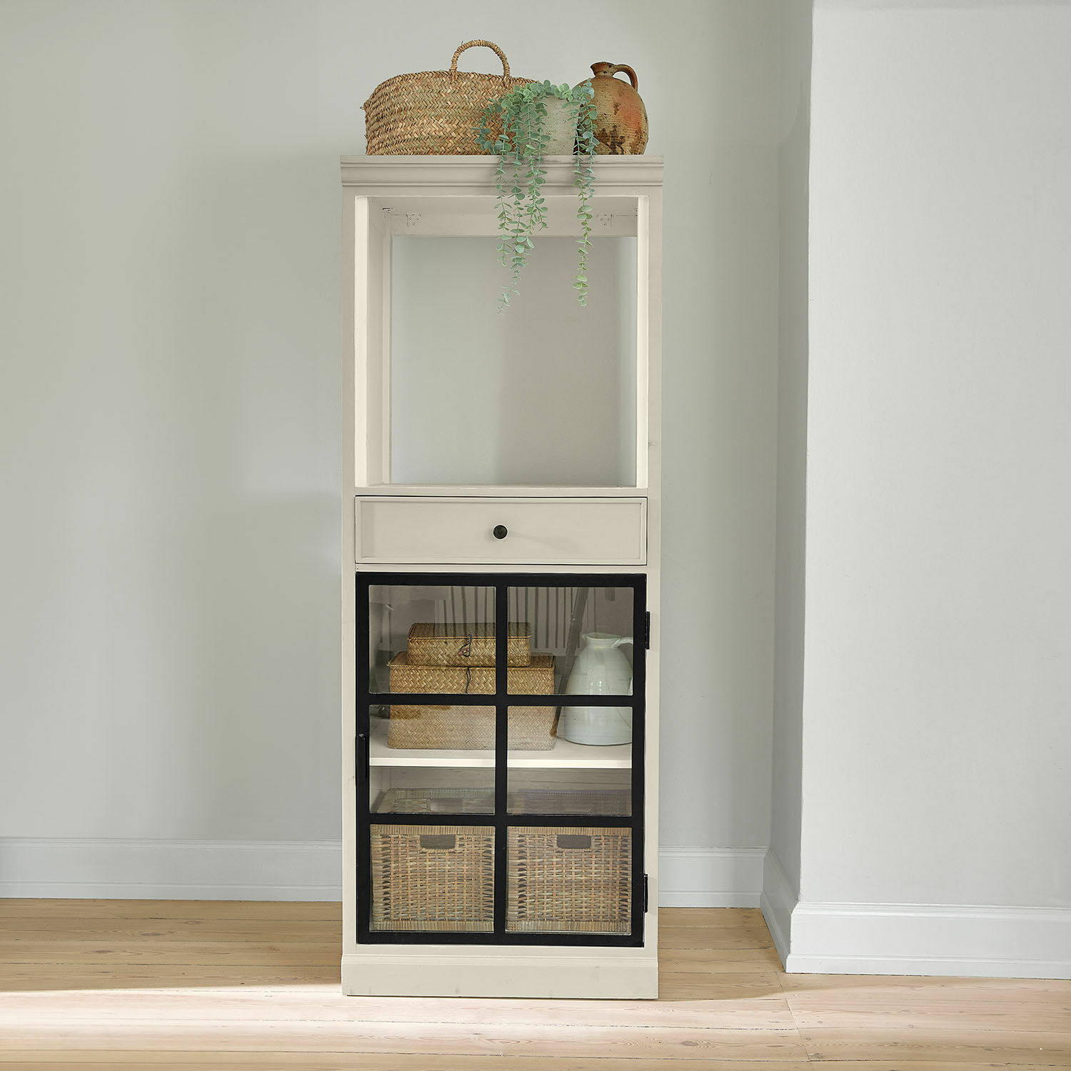 Weiße Holzvitrine mit schwarzen Metalltüren und geflochtenen Körben zur Aufbewahrung