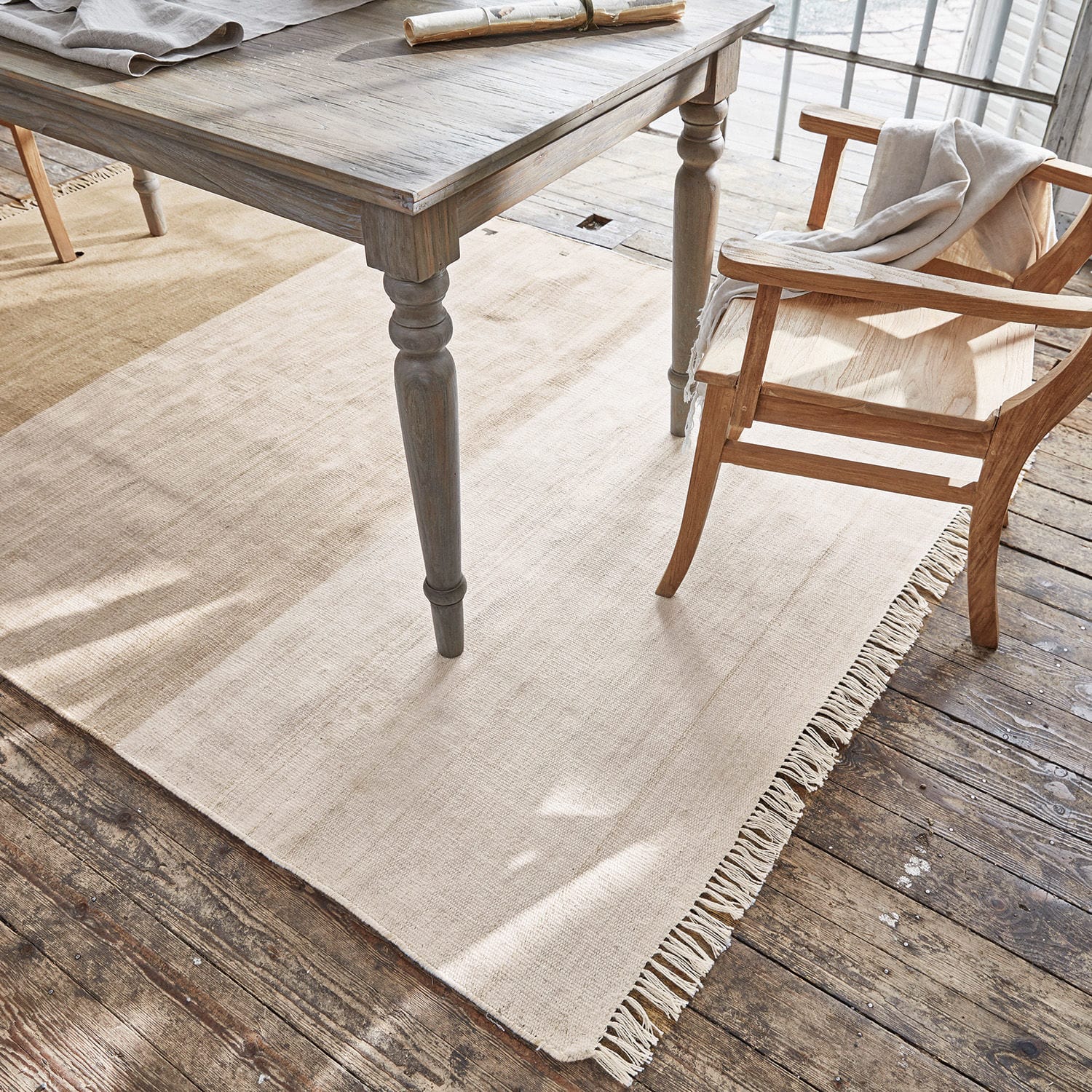 Beiger Teppich mit Fransen unter einem Holztisch und Stuhl, Naturmaterial, Wohnaccessoire