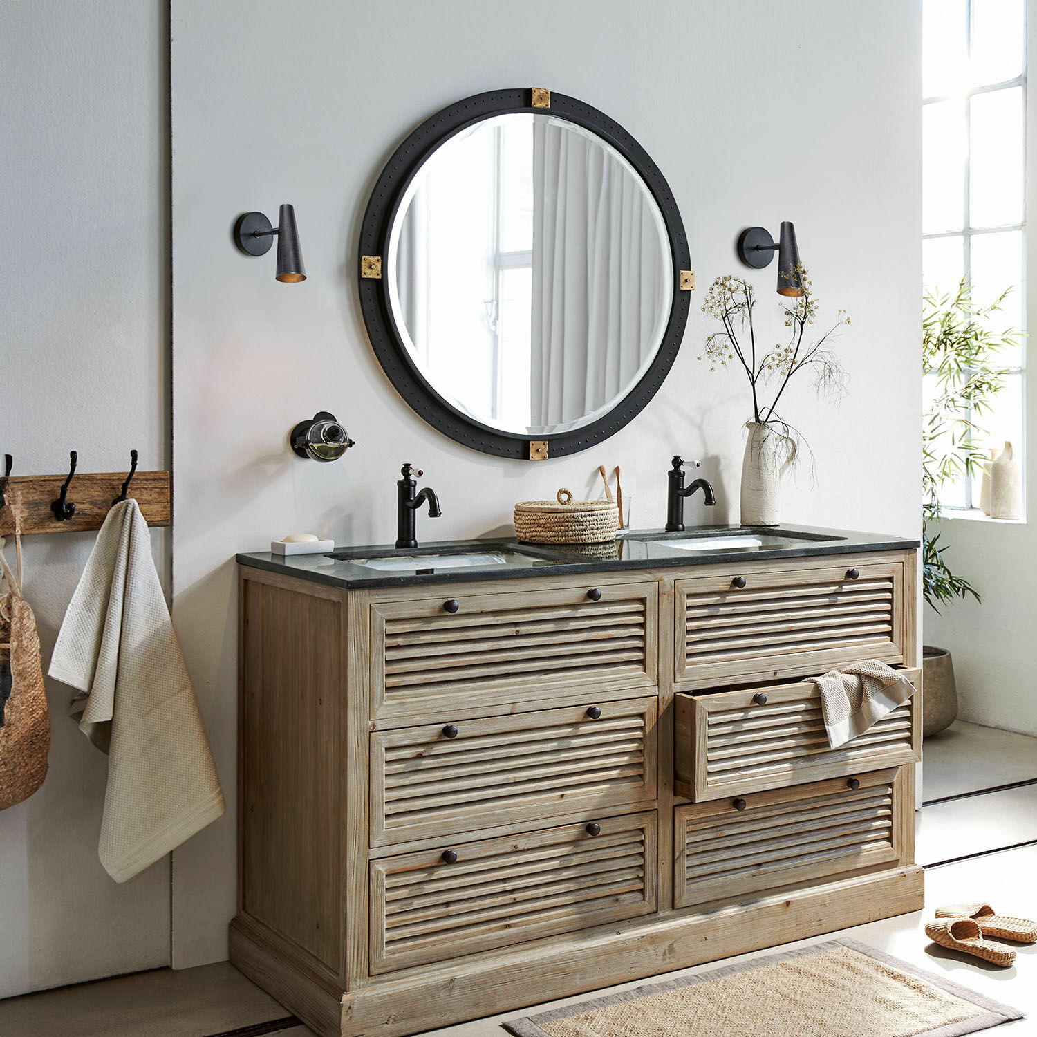 Holz-Badezimmerschrank mit zwei schwarzen Wasserhähnen und rundem Spiegel mit schwarzem Rahmen
