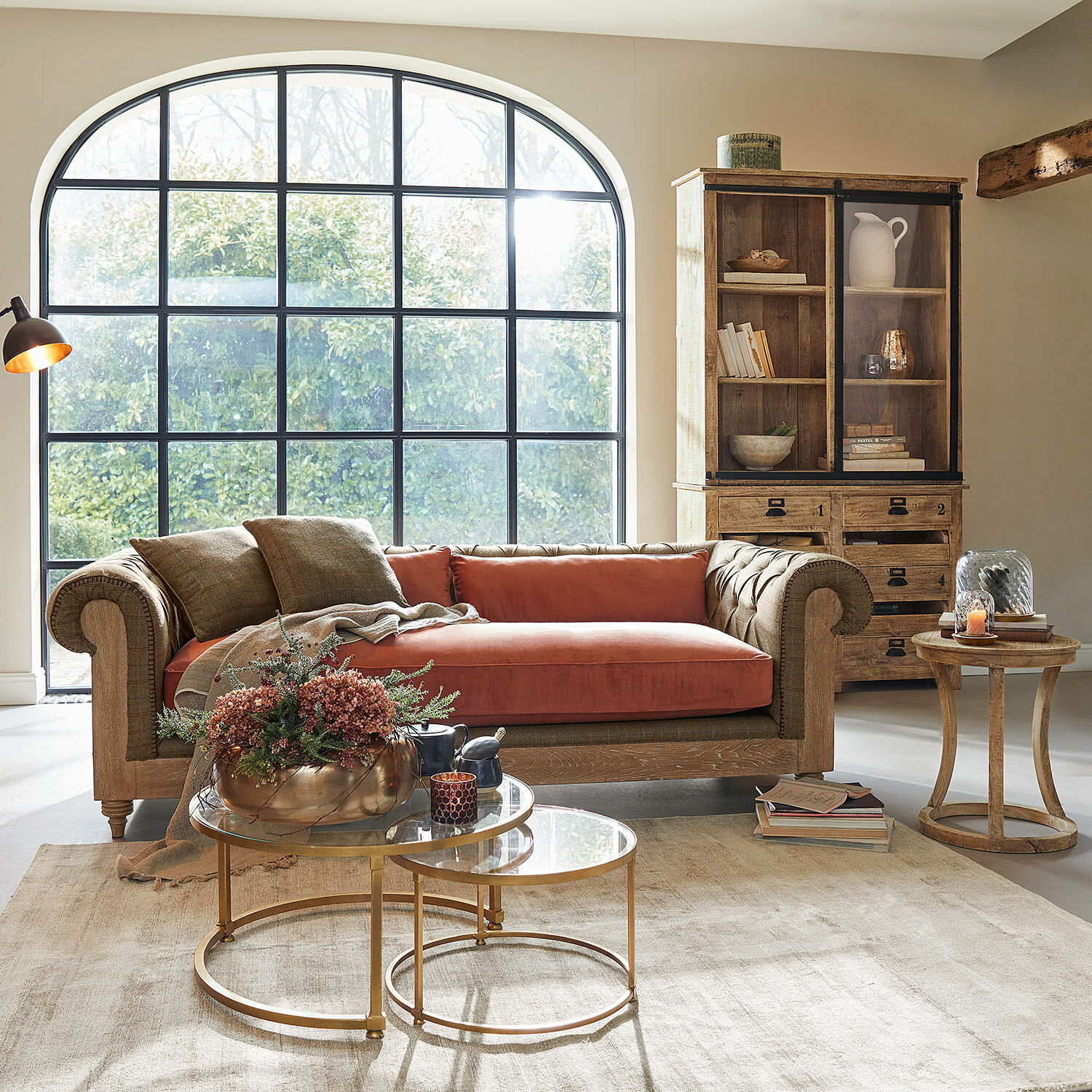Wohnzimmer mit braunem Holzsofa und orangefarbenem Kissen, Glastische mit goldenem Metallgestell