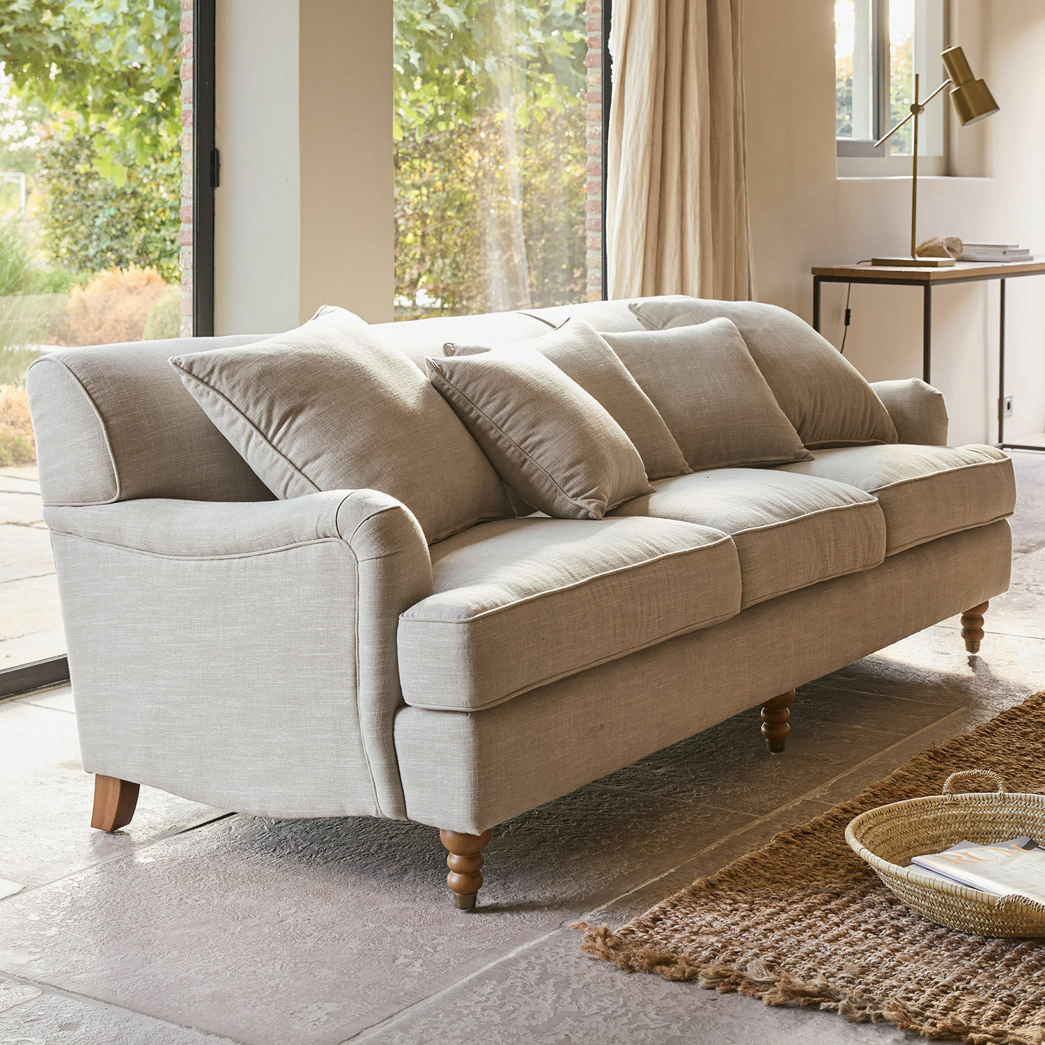 Beige bezogener Sofa mit Kissen und Holzbeinen in hellem Wohnzimmer mit Teppich