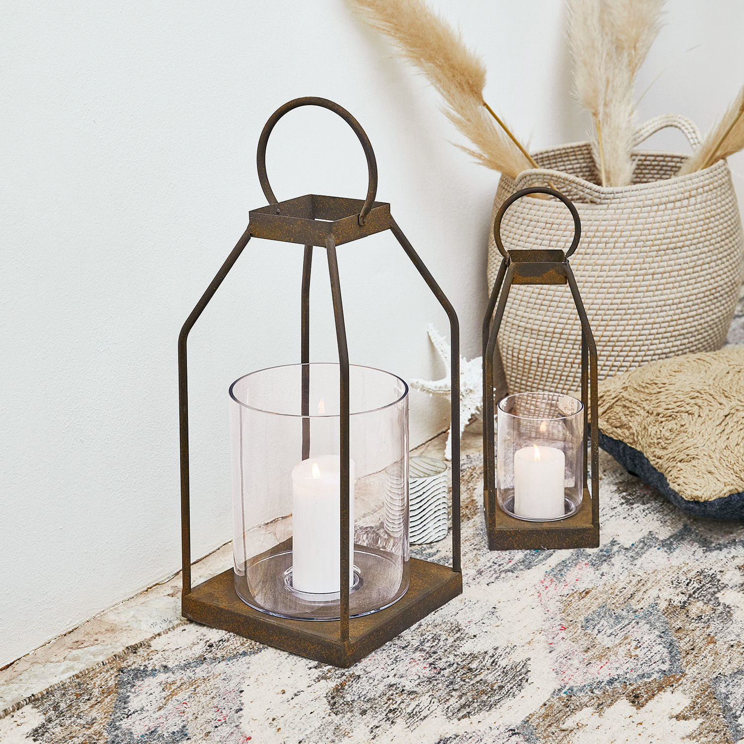 Set aus zwei rostfarbenen Metalllaternen mit klarem Glas und weißen Kerzen im Inneren