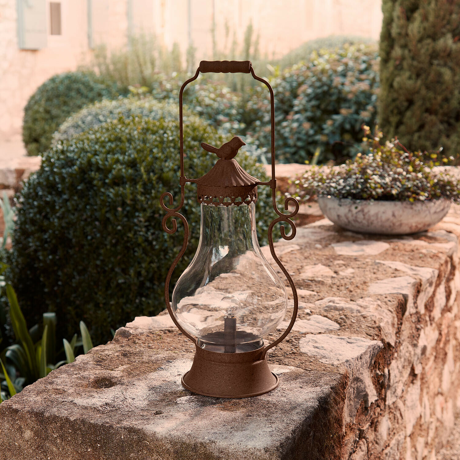 Rustikale braune Metalllaterne mit Glasaufsatz auf einem Steinmauer im Garten