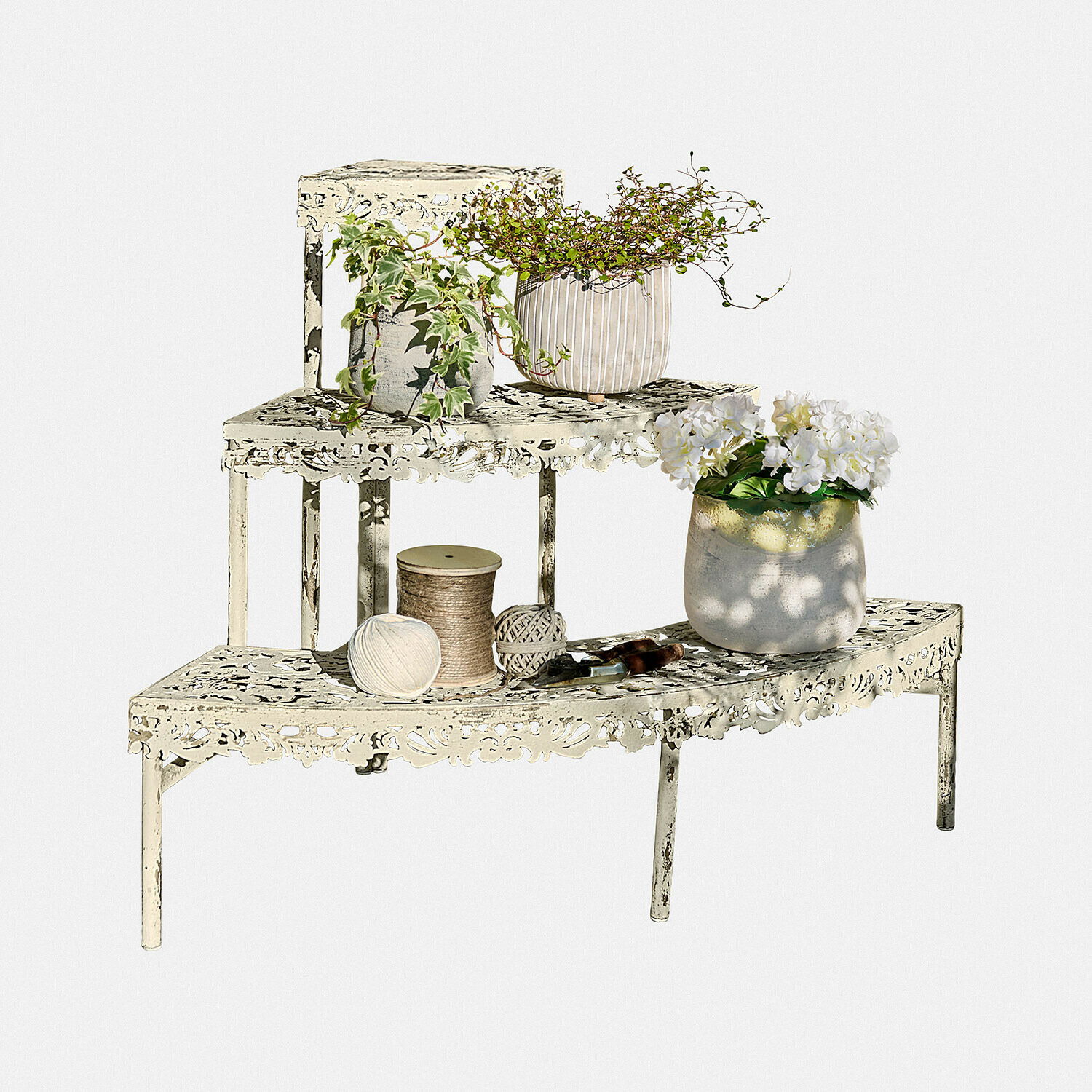 Pflanztreppe Cresselay Metallregal in Creme mit filigranem Muster, Pflanzen und Gartengeräten vor weißem Hintergrund