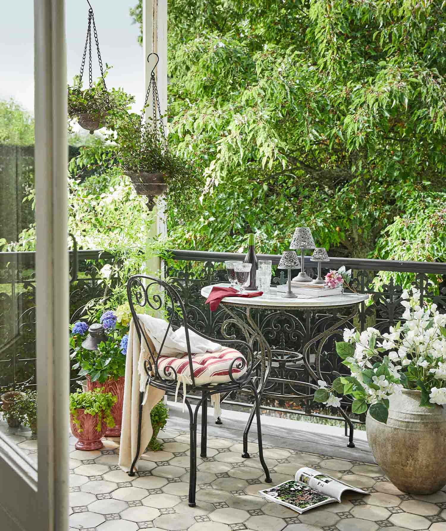 Balkon mit schmiedeeisernem Tisch und Stuhl mit gestreiftem Kissen, umgeben von grünen Pflanzen und Blumentöpfen