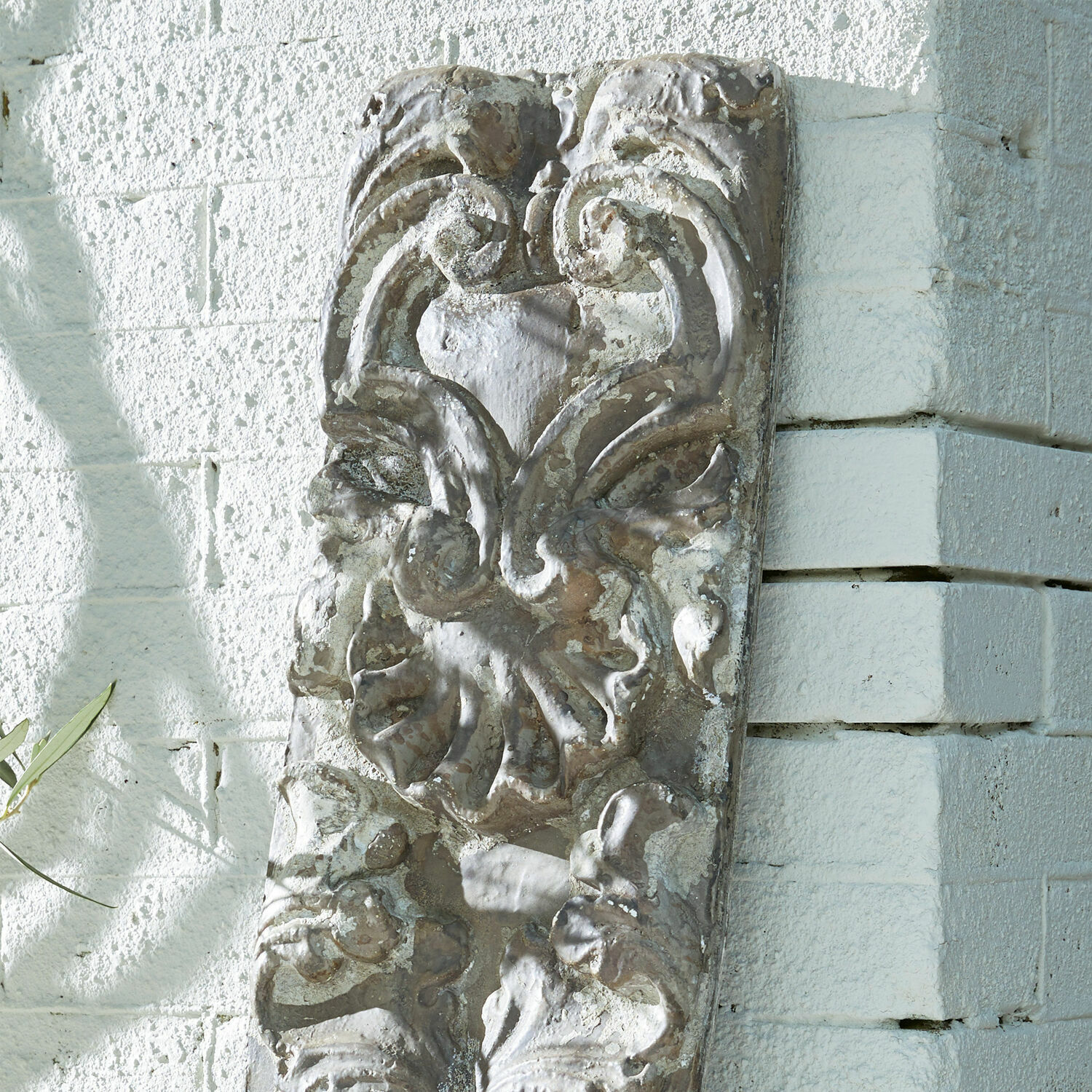 Verziertes graues Steingrelief mit Pflanzenmotiv an weißer Wand, dekoratives Wandobjekt